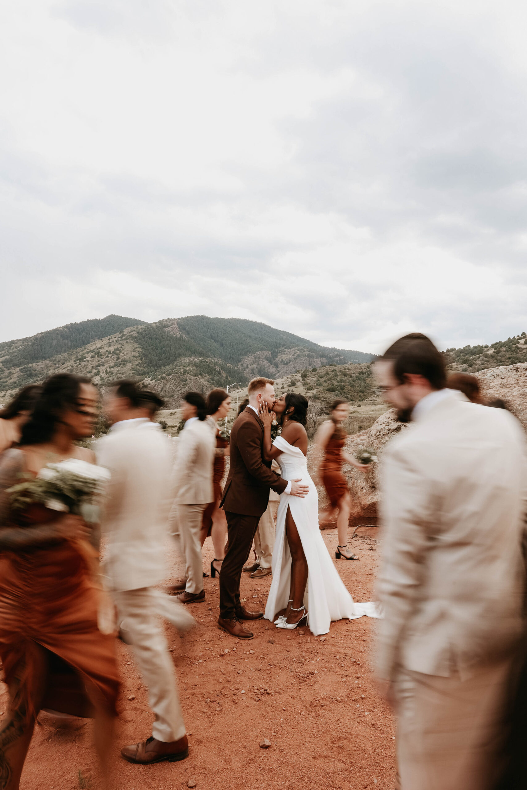bridal couple kissing and blurry bridal party walking around them 