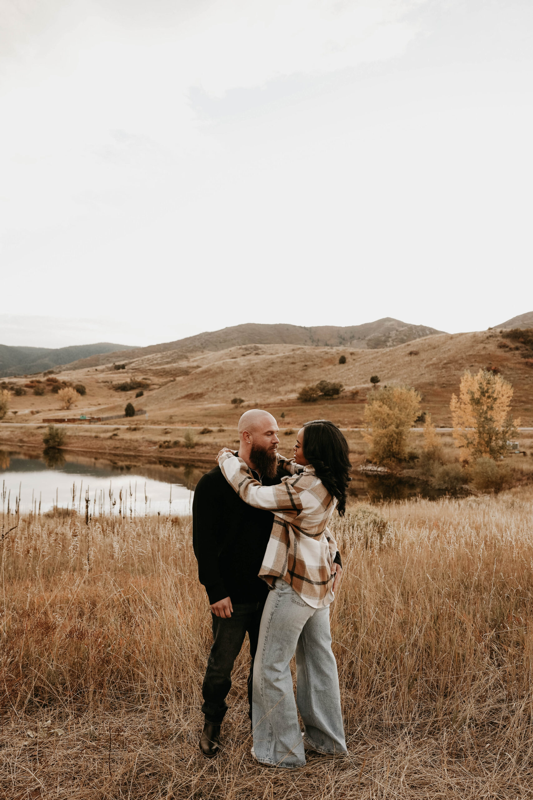 newly engaged couple holding and looking at each other with fall mountain scenery in background