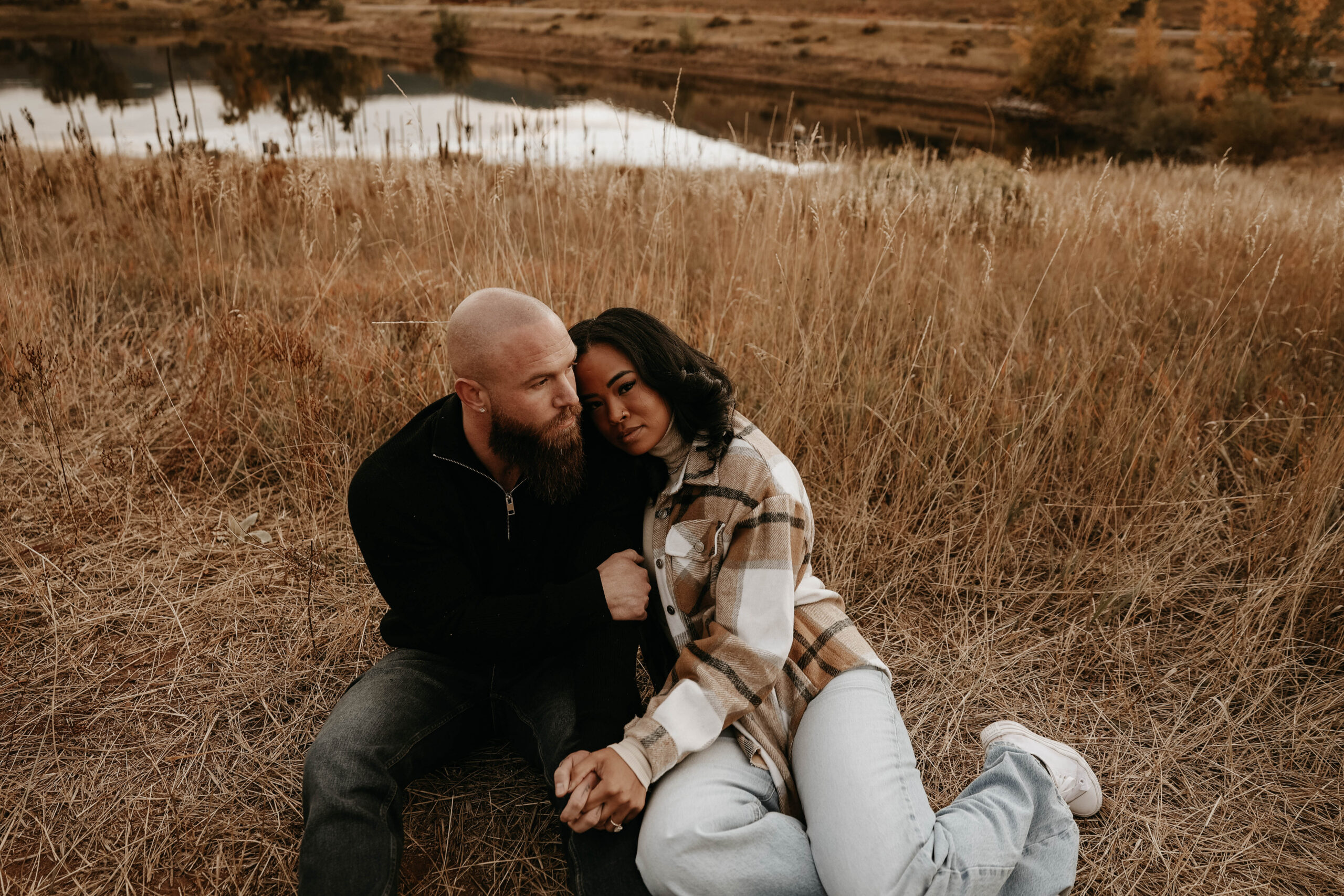 photographers picture of newly engaged couple sitting in the dried grass holding each other during their engagement photos 