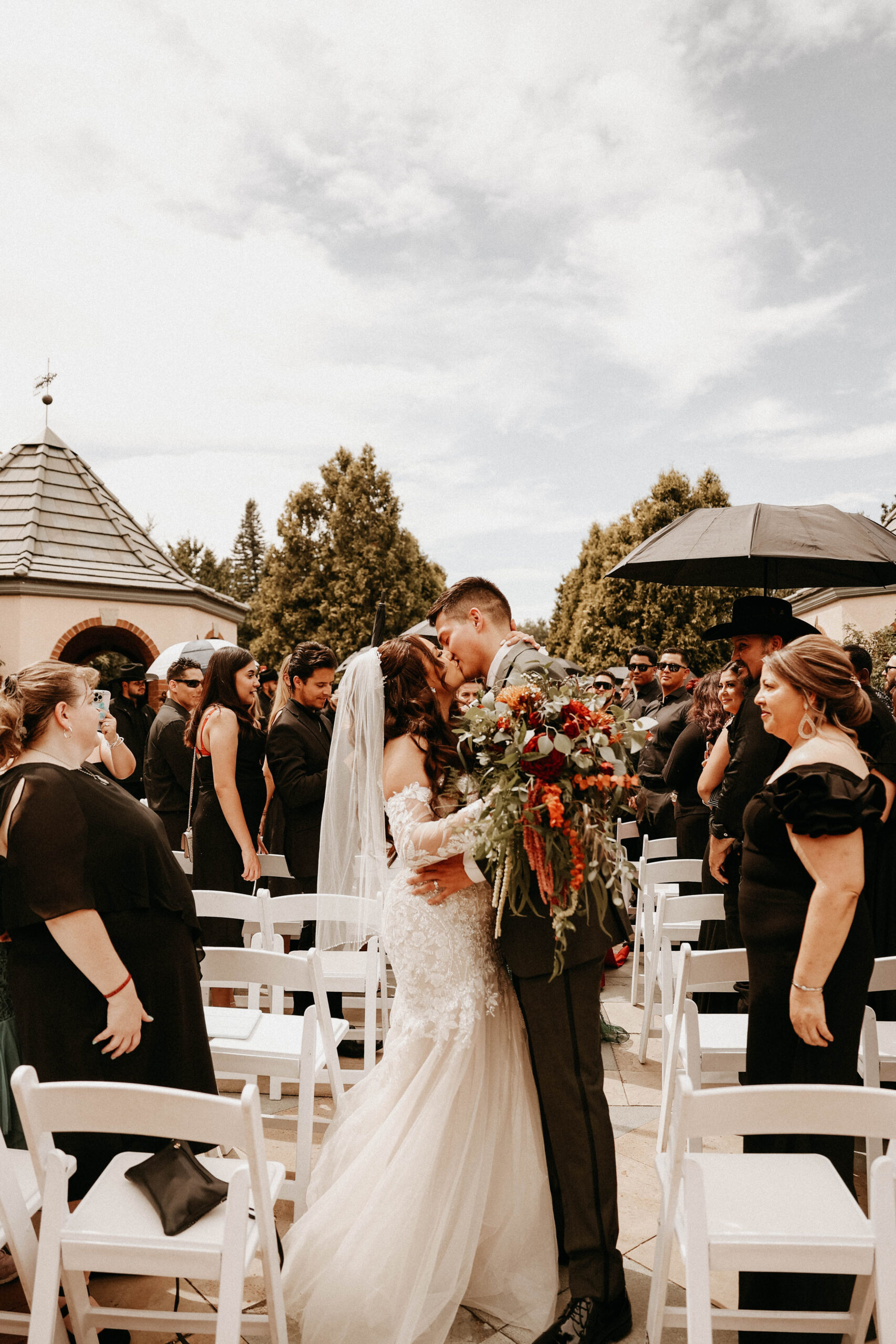 bride and groom kissing at the end of the altar with all black dressed guests surrounding them 