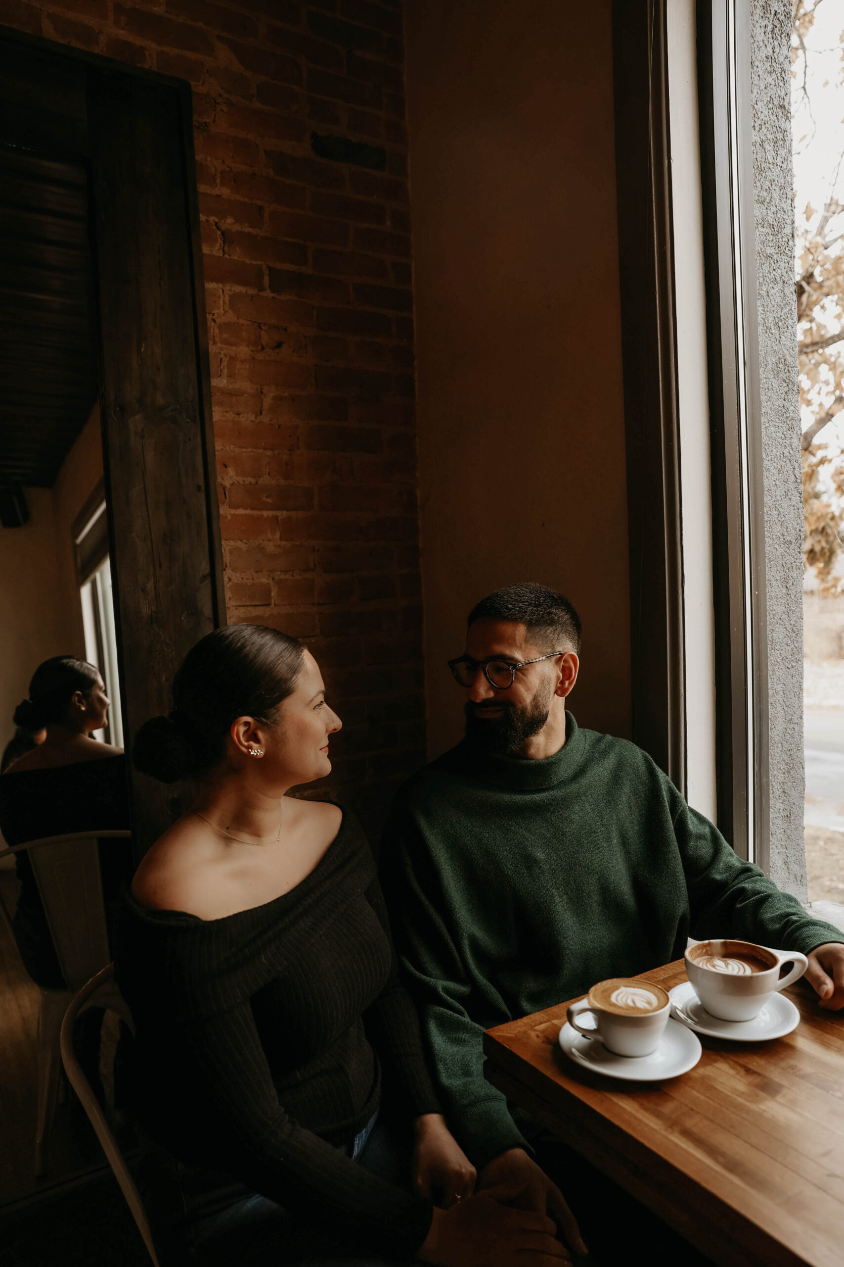 couple sitting at coffee shop table with their coffee and looking at each other 