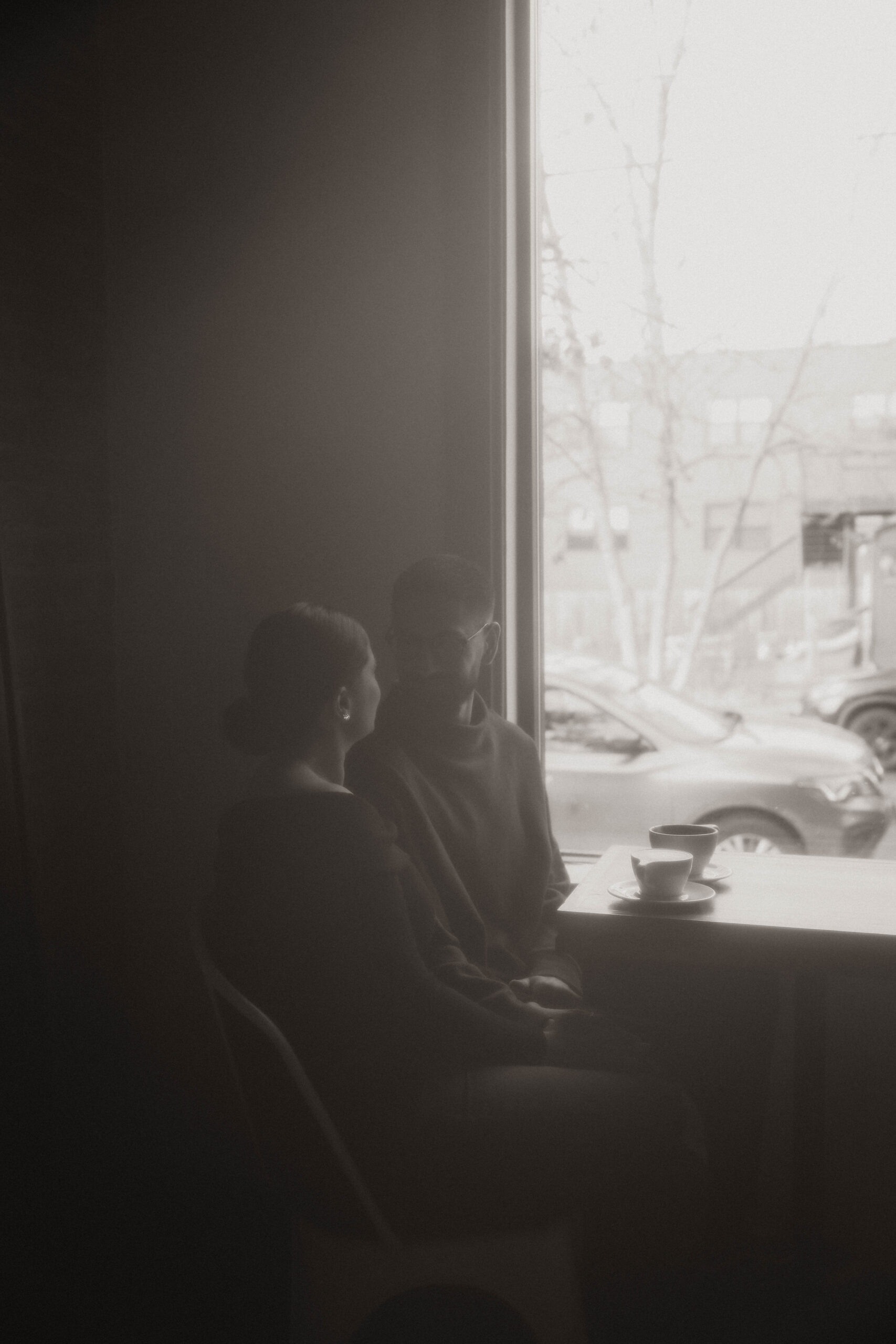 grainy black and white of couple sitting at a table at a coffee shop for engagement photos 