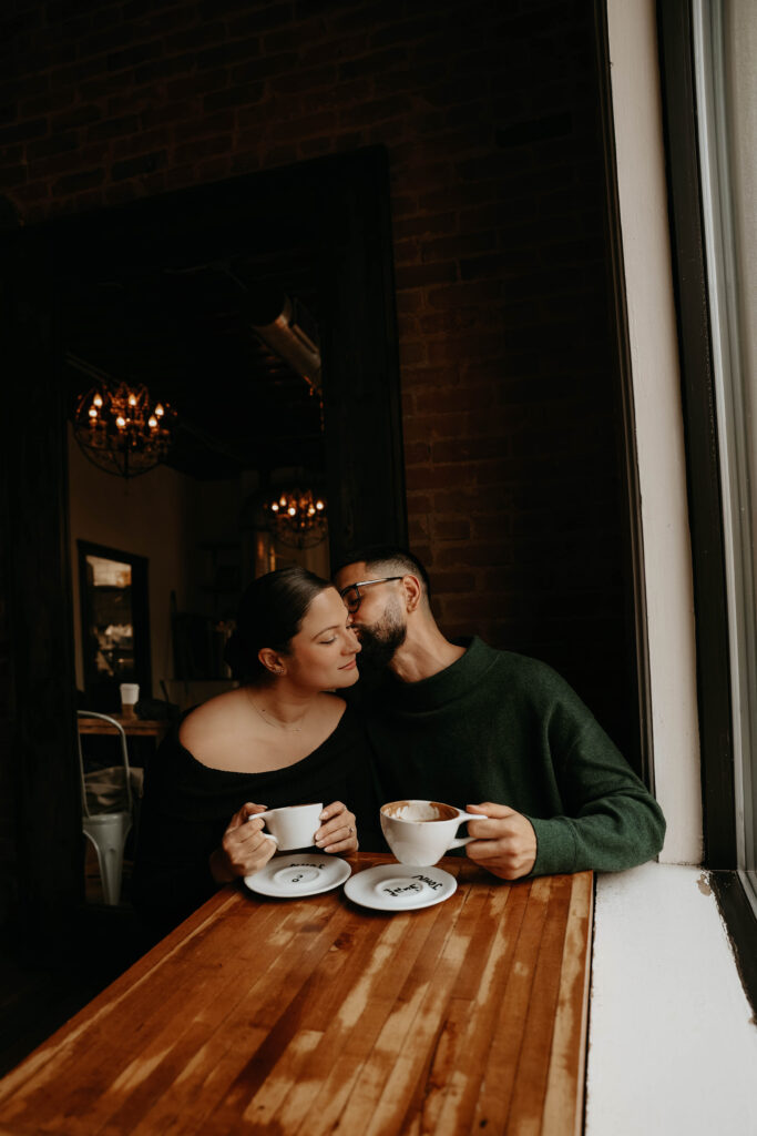 couple kissing at the table with their coffee during their engagement photos 
