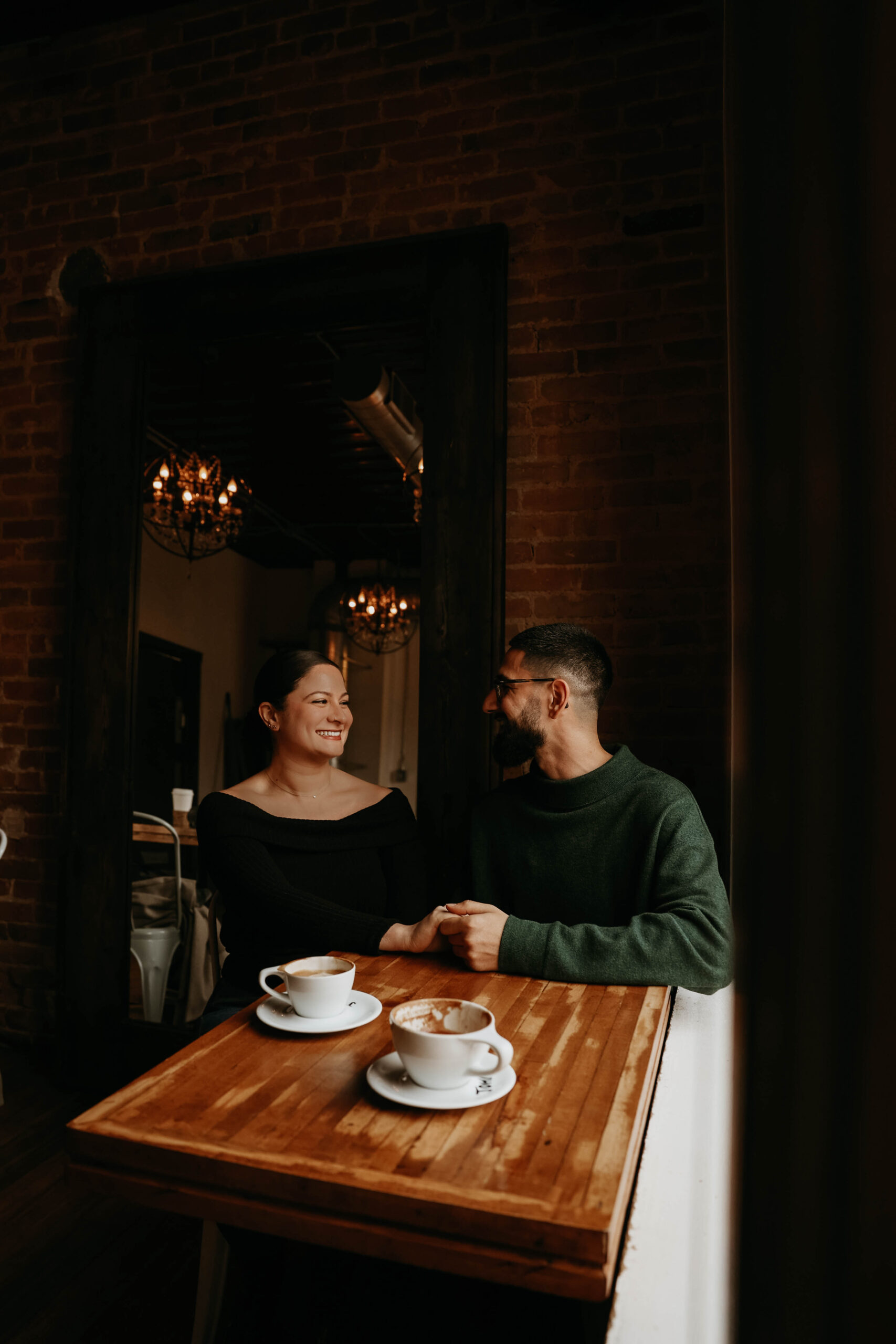 couple sitting at a coffee shop table smiling at each other 