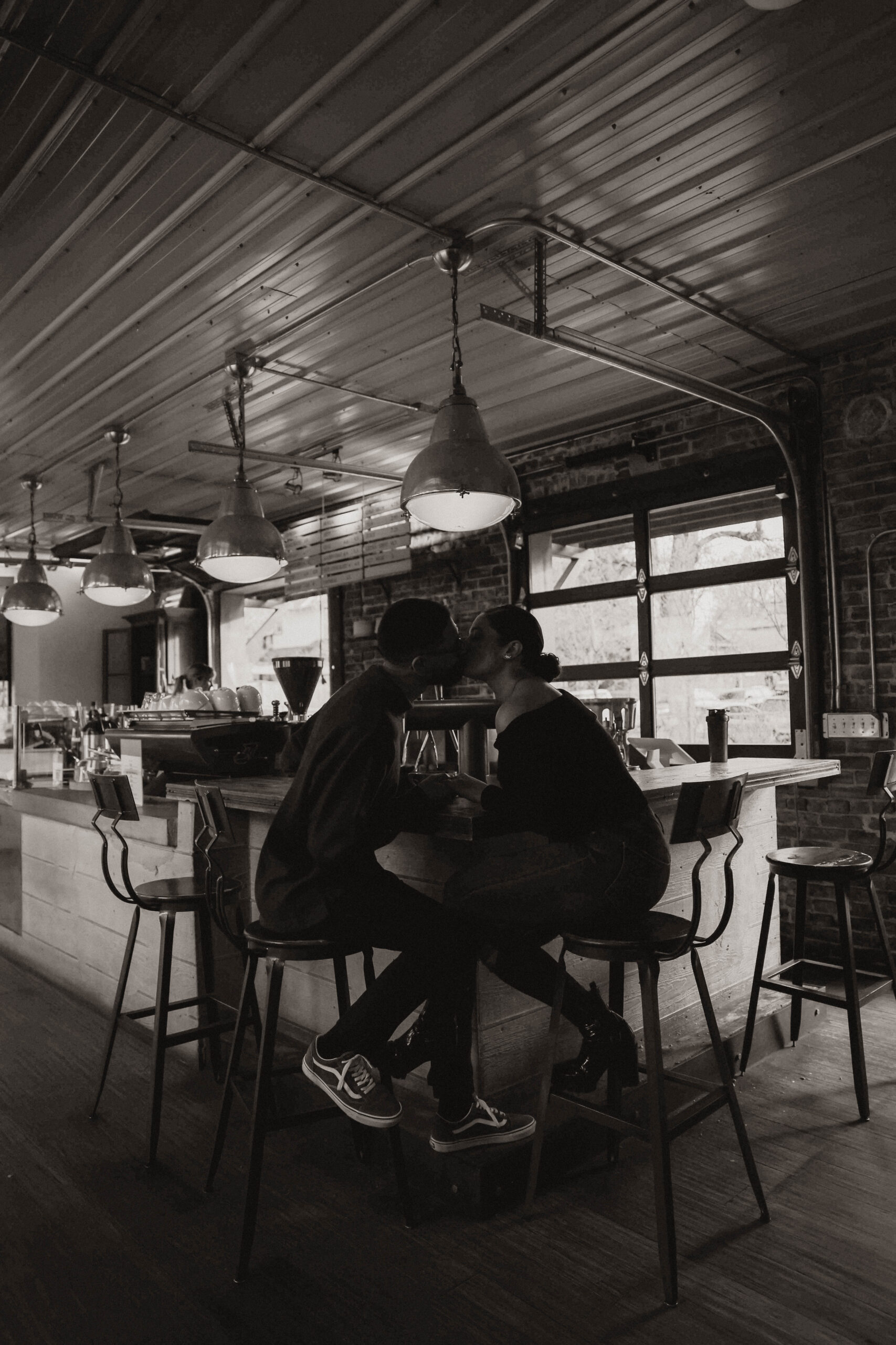 engaged couple at their engagement photo location, a coffee shop, sitting at the bar and kissing 