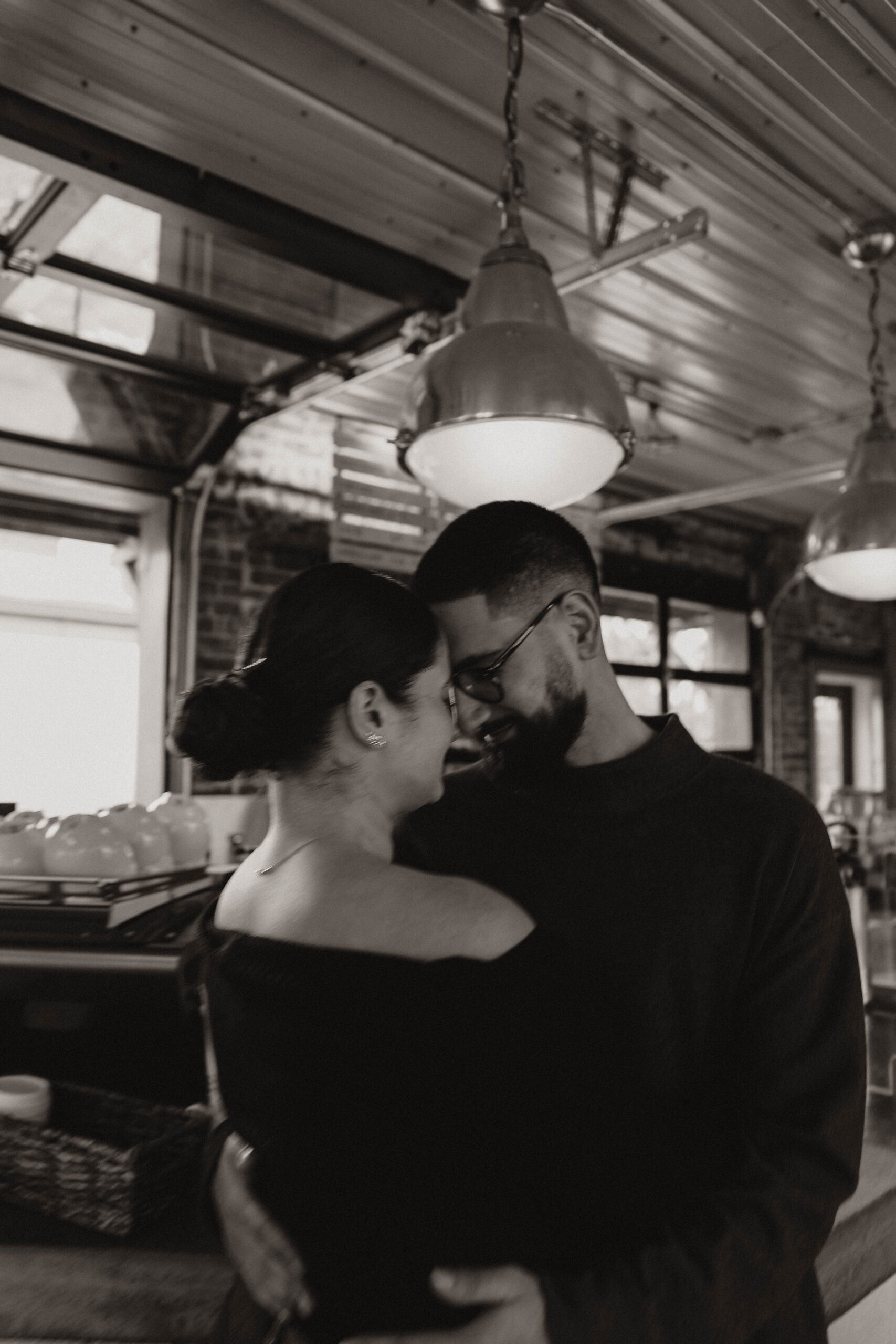 blurry photo of engaged couple at their engagement photo location, a coffee shop, standing with their foreheads together and smiling 