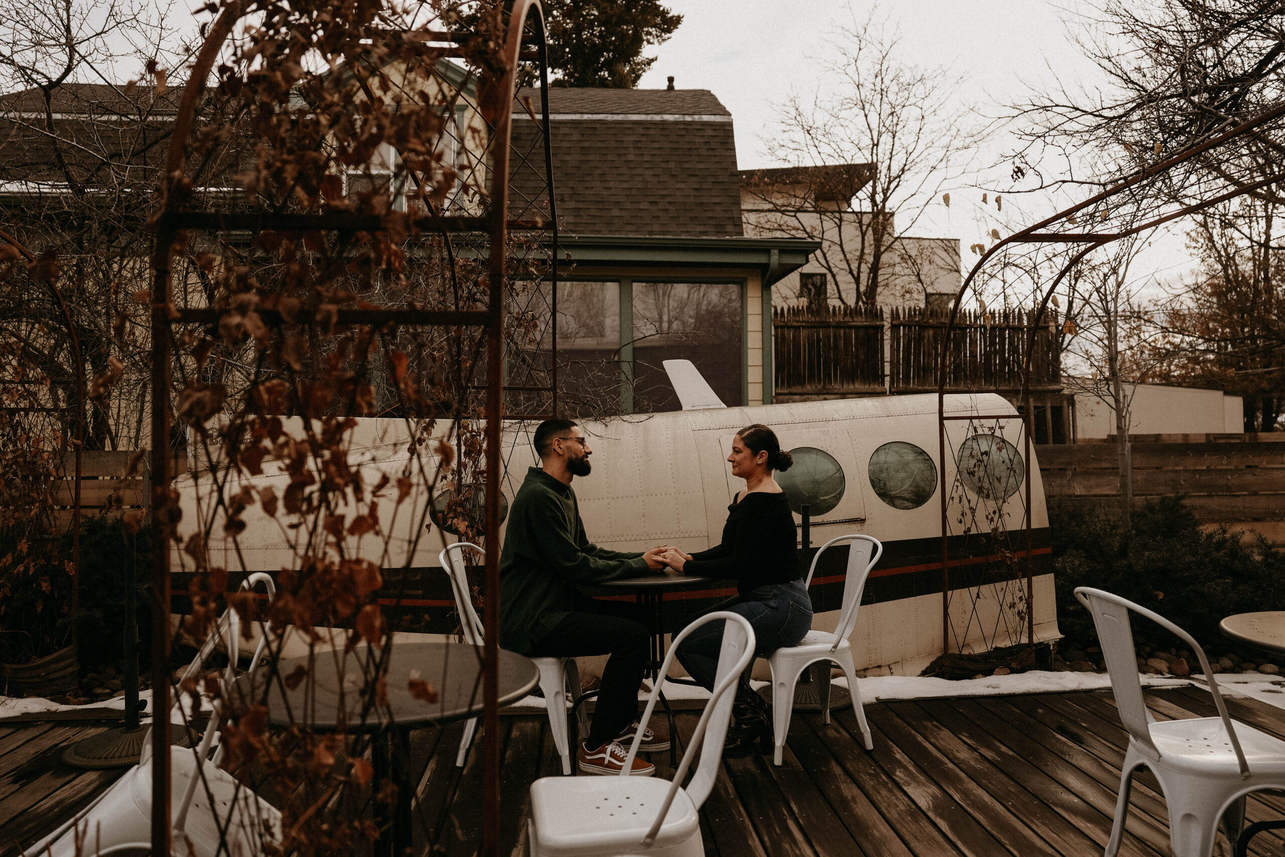 couple sitting at a table on the patio of coffee shop in front of parts of a plane 