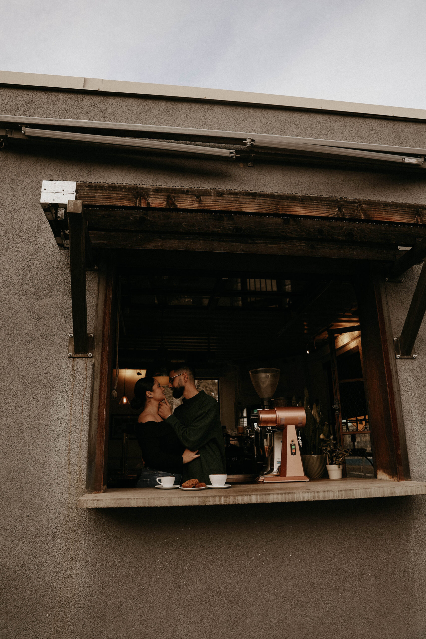 engaged couple at their engagement photo location, a coffee shop, standing in the window holding each other 