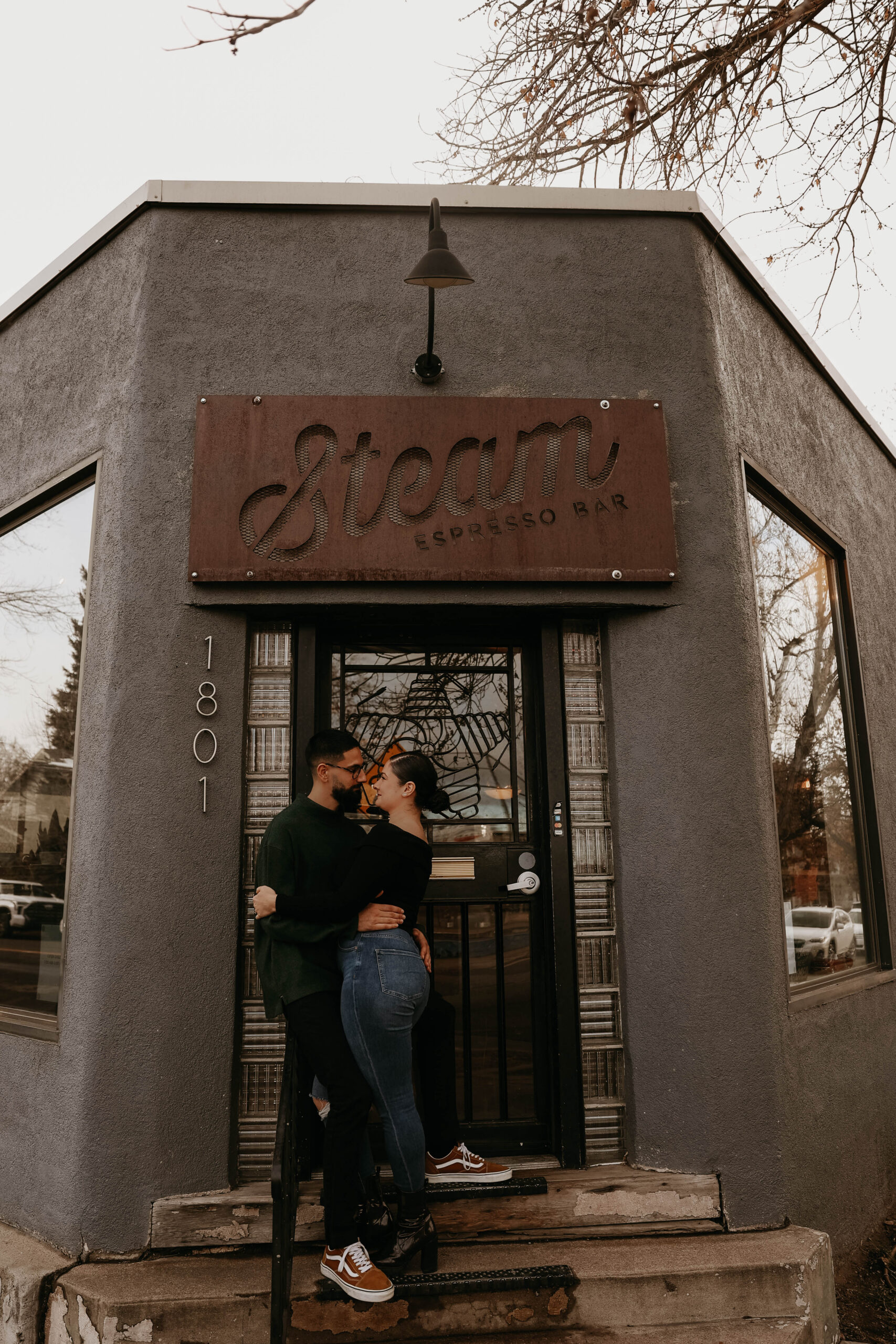 couple standing outside of steam espresso bar, there engagement photo location of choice