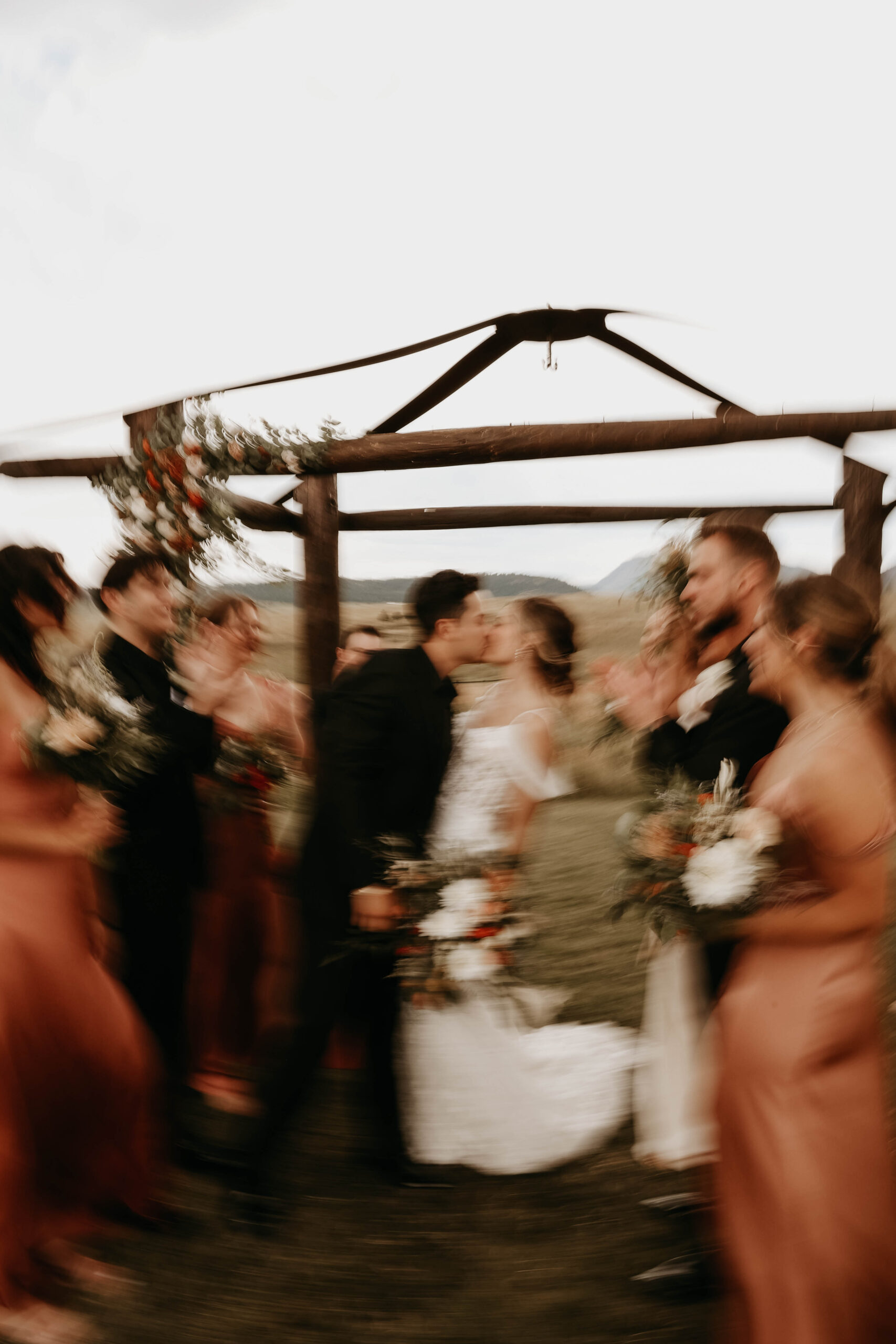 blurry photo of wedding party and bride and groom kissing 