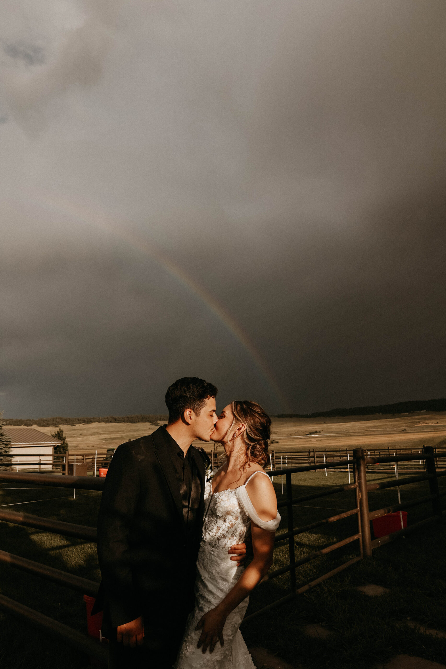 bridal couple kissing with a rainbow in the background