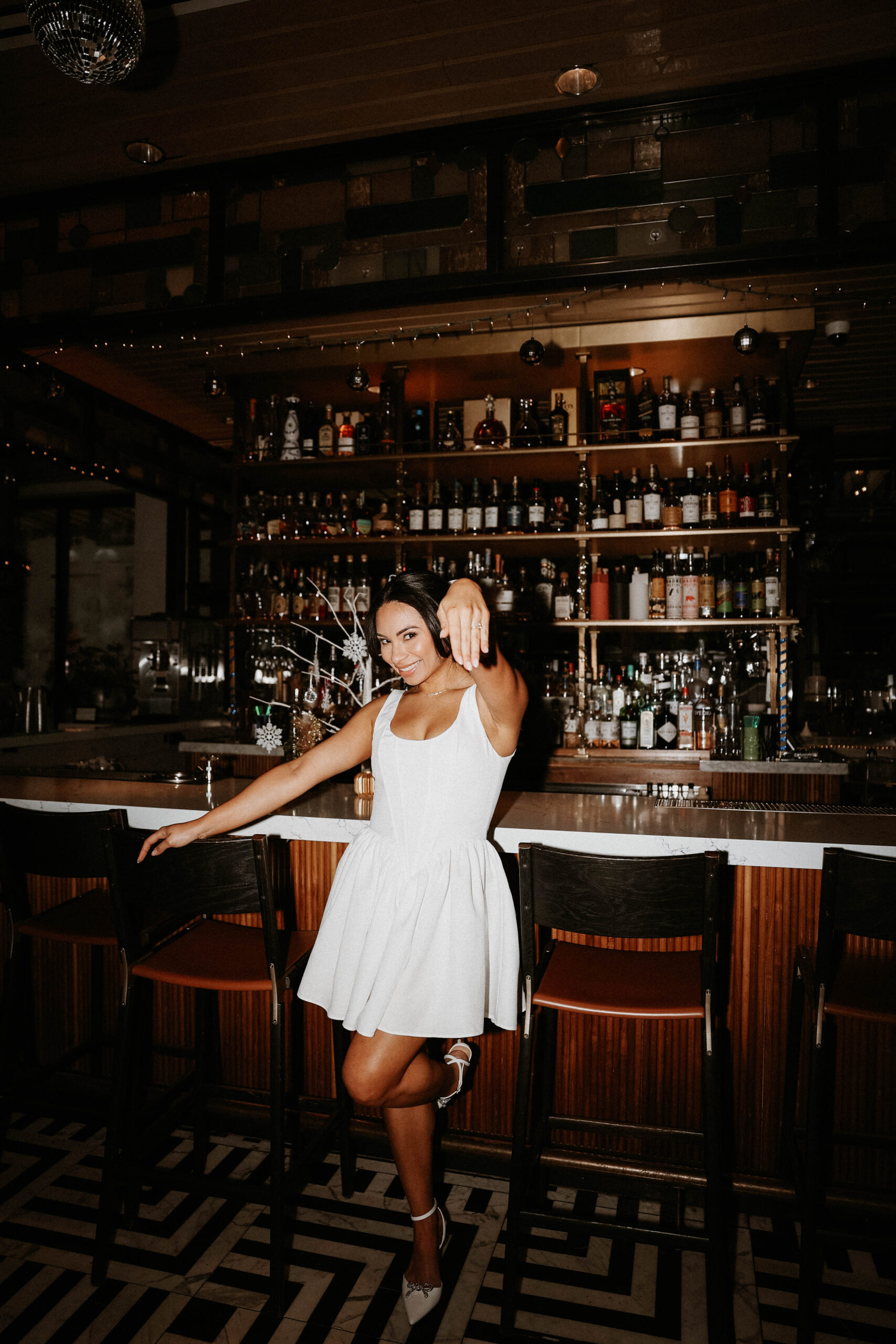 bride to be standing at the bar holding out her hand with her ring on it 