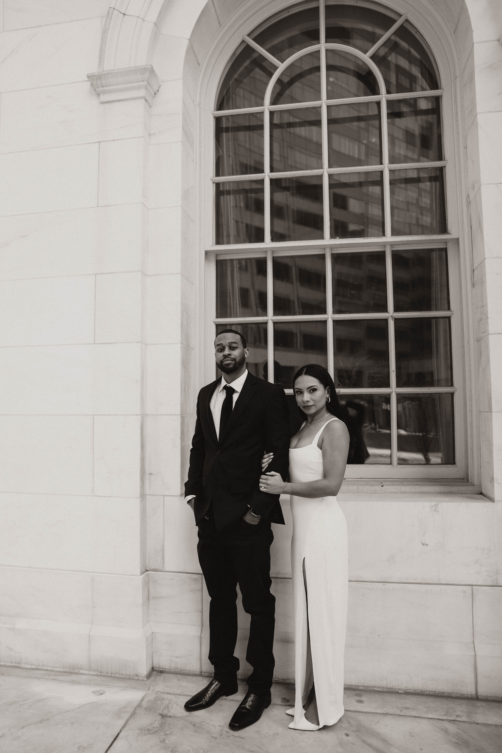 black and white of engaged couple in formal attire standing next to the courthouse 