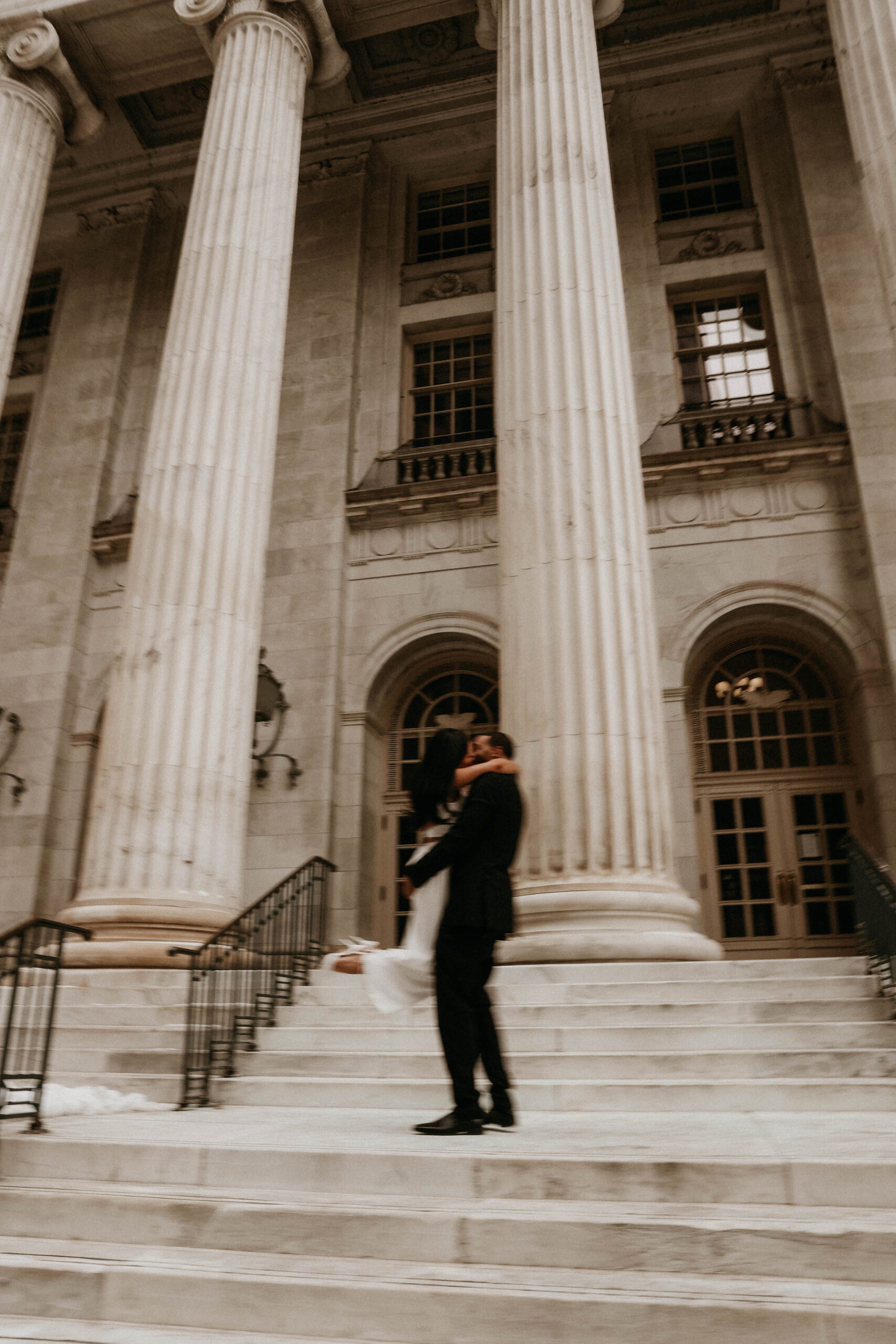 blurry photo of fiance holding other fiance and swinging her around in front of the courthouse, bringing their unique engagement shoot ideas to life 