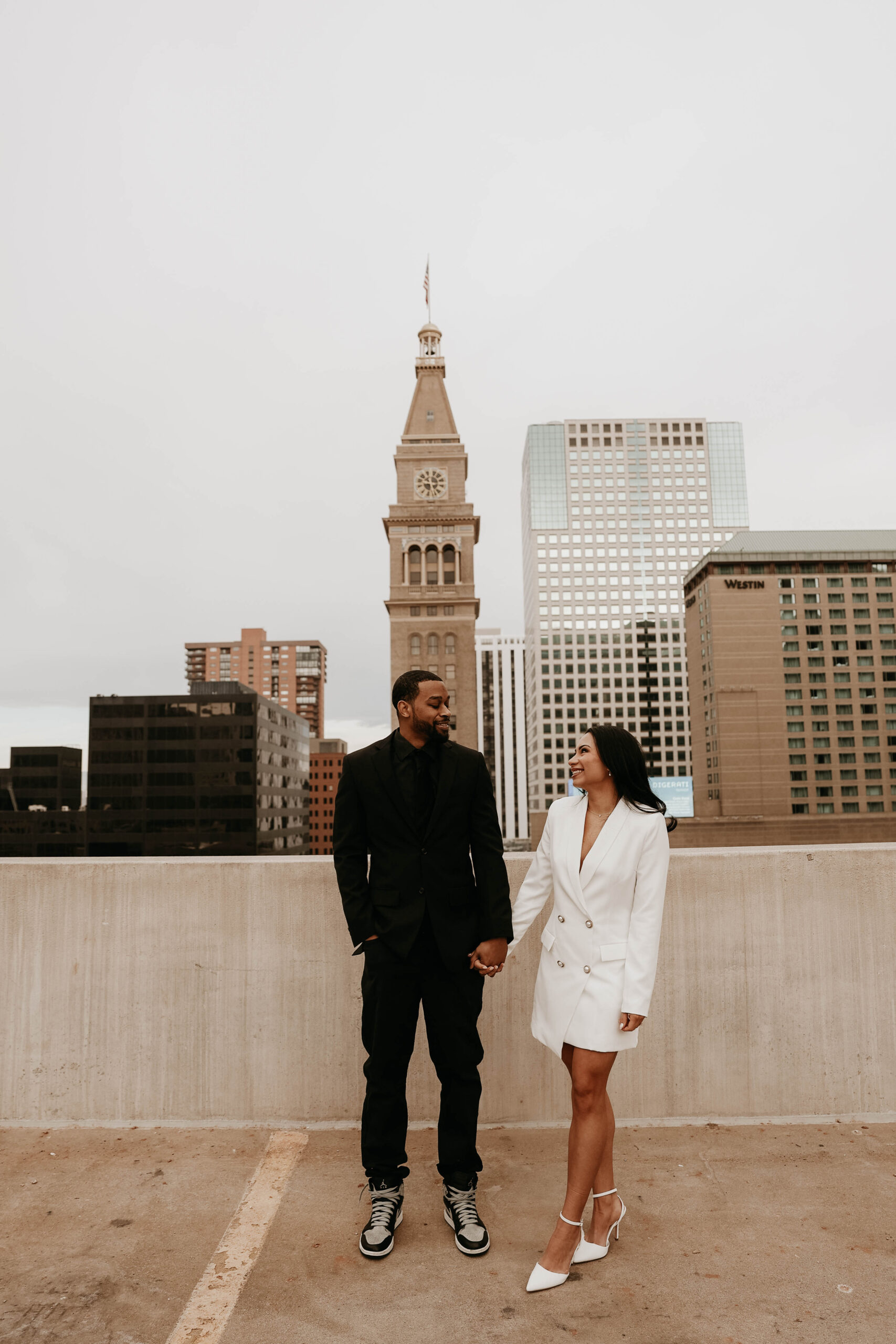 newly engaged couple holding hands on a rooftop expressing their unique engagement shoot ideas