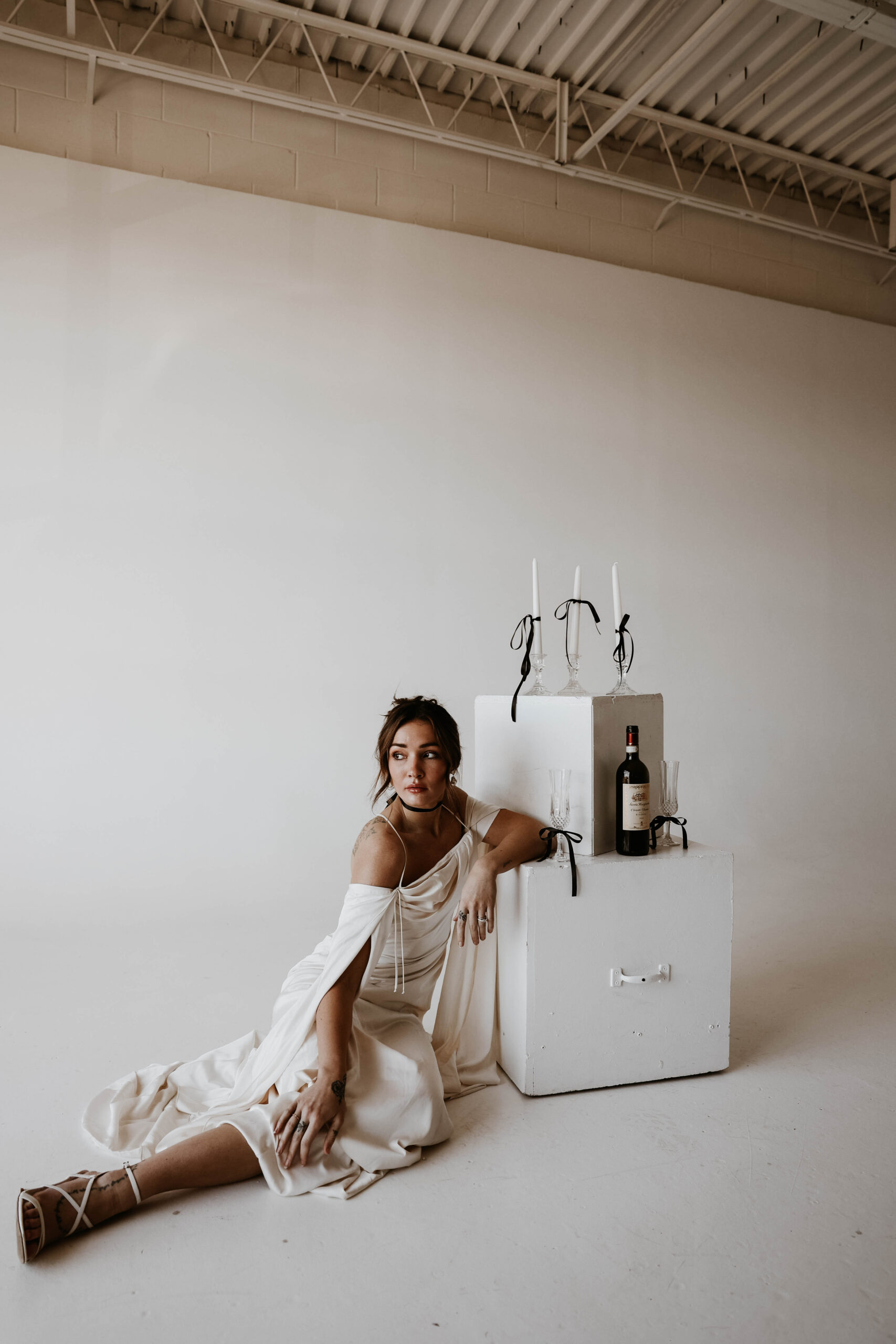 studio bridal photography of bride sitting next to boxes with candles and wine on them 