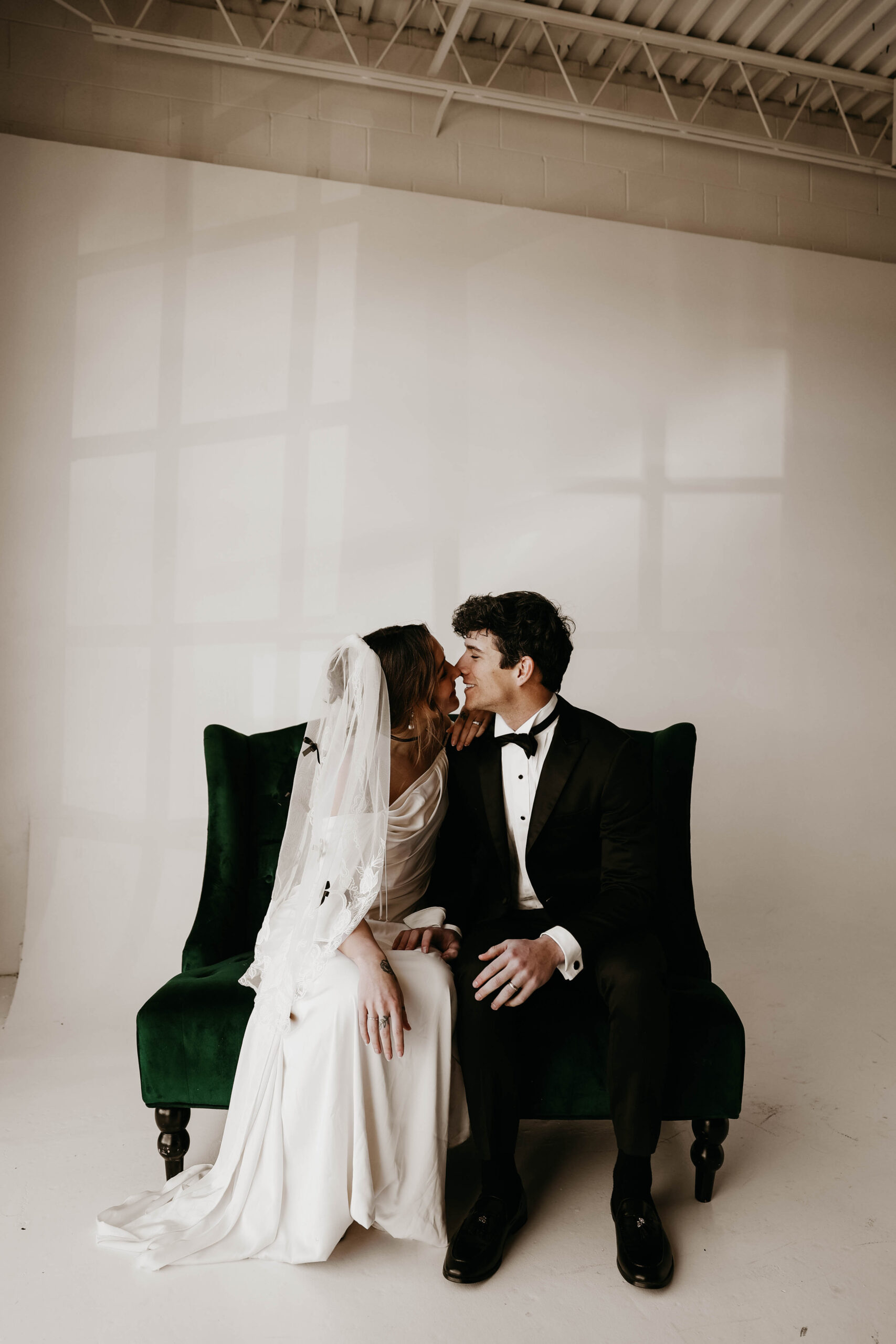 bride and groom sitting on a chair and laughing as they almost kiss 