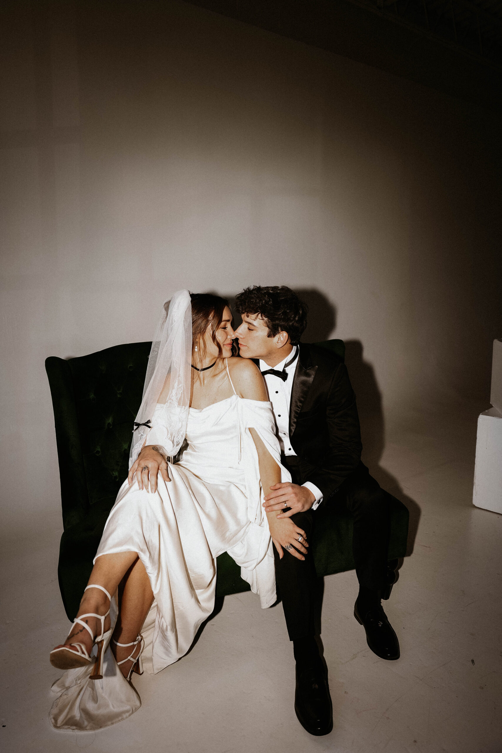 studio bridal photography of wedding couple sitting on a chair with their noses together 