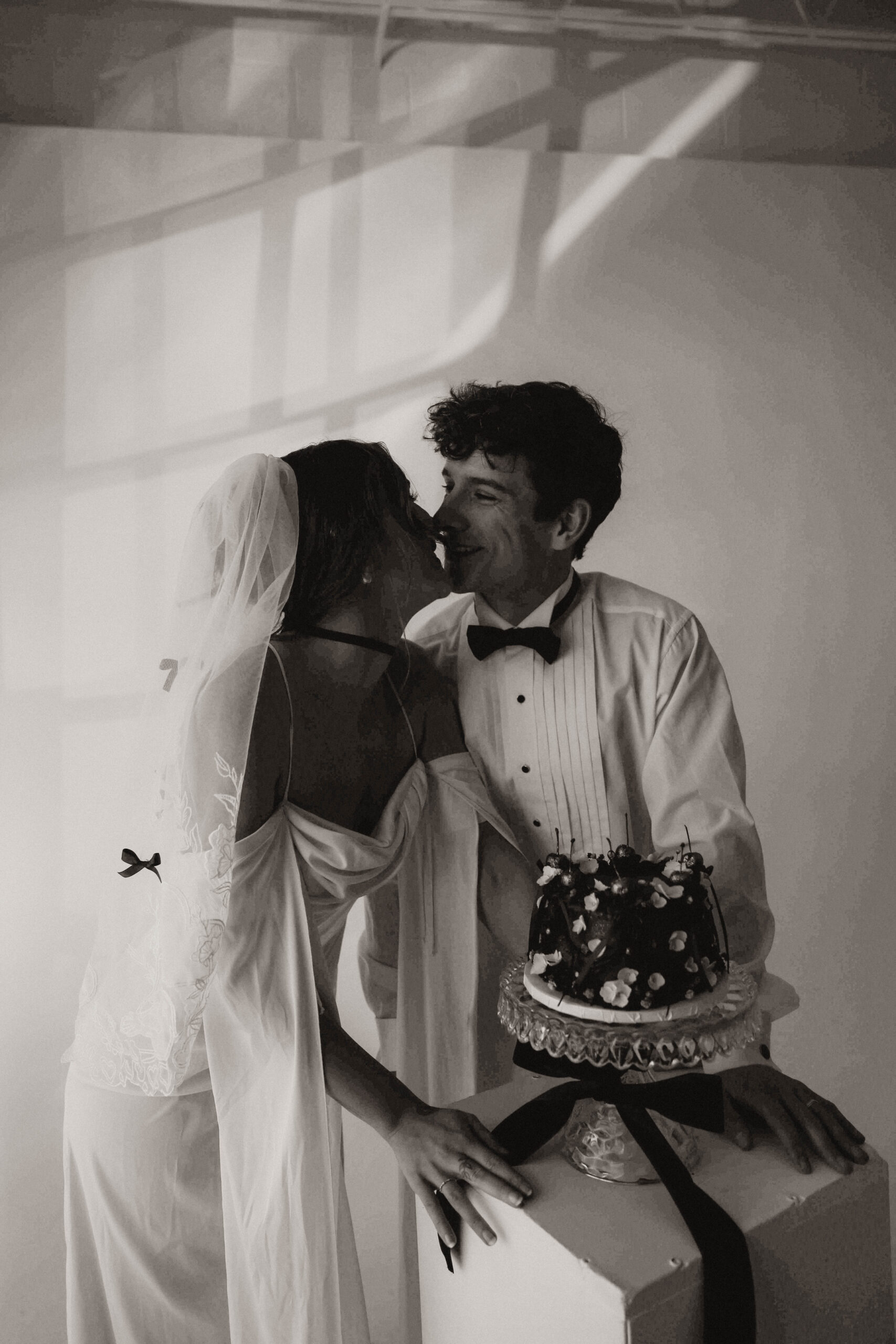 studio bridal photography of bride and groom smiling next to their cake 