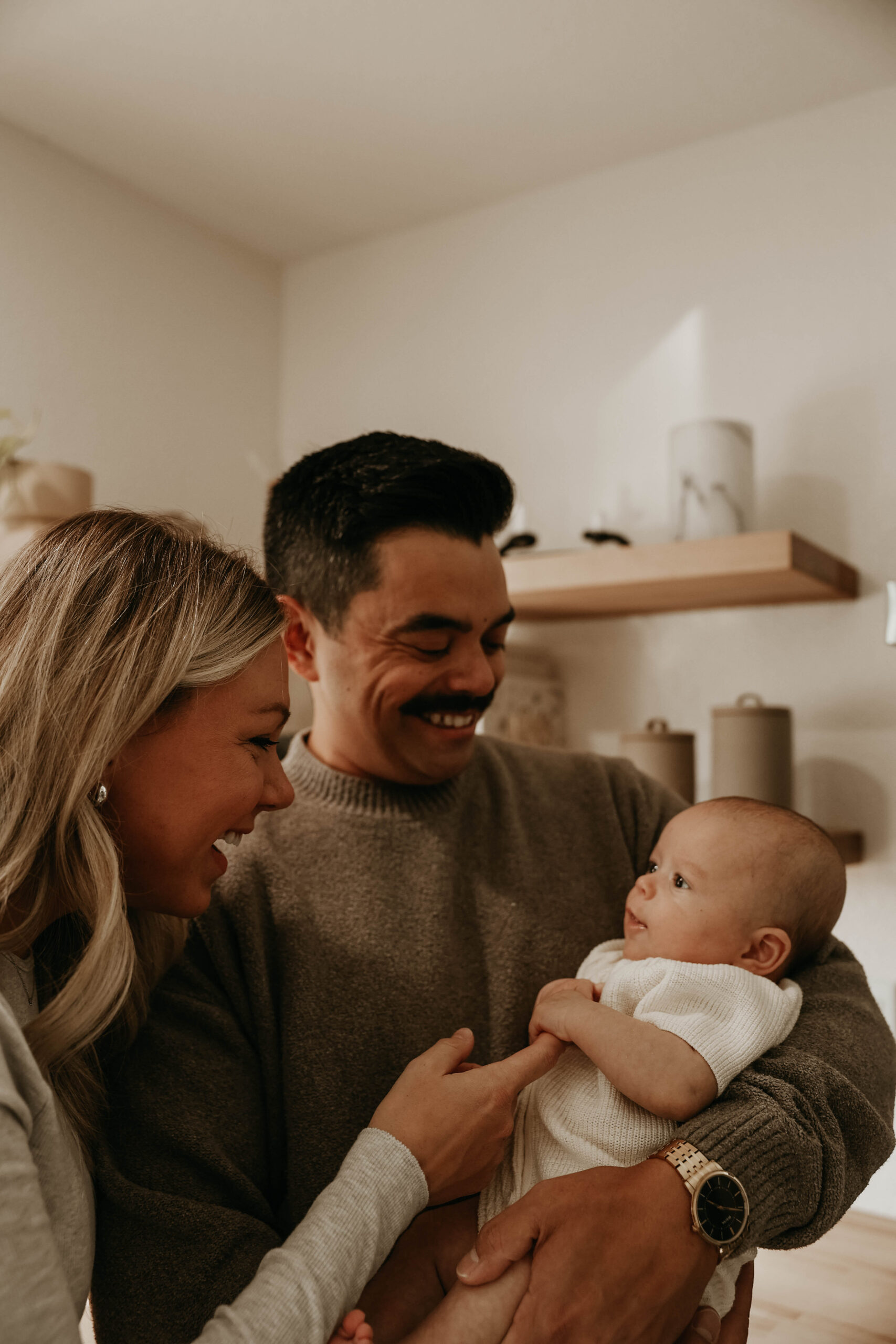 new parents smiling and talking to their baby during in-home family photos 
