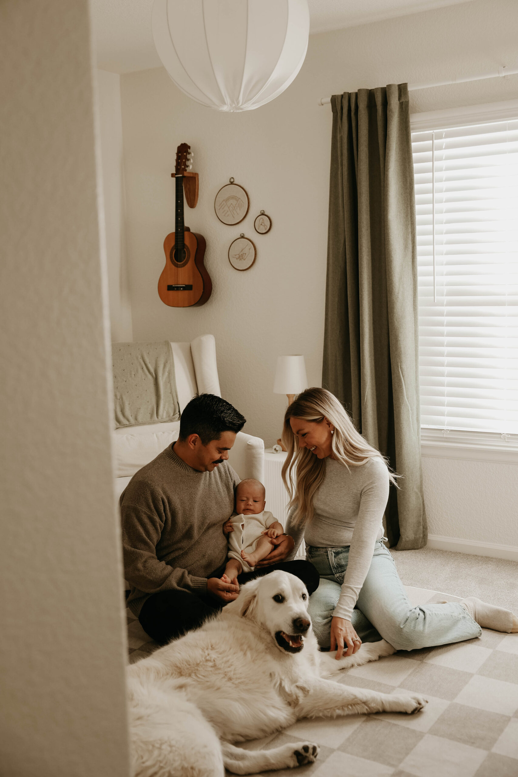 new parents sitting on the floor with their baby and their dog during in-home family photos 