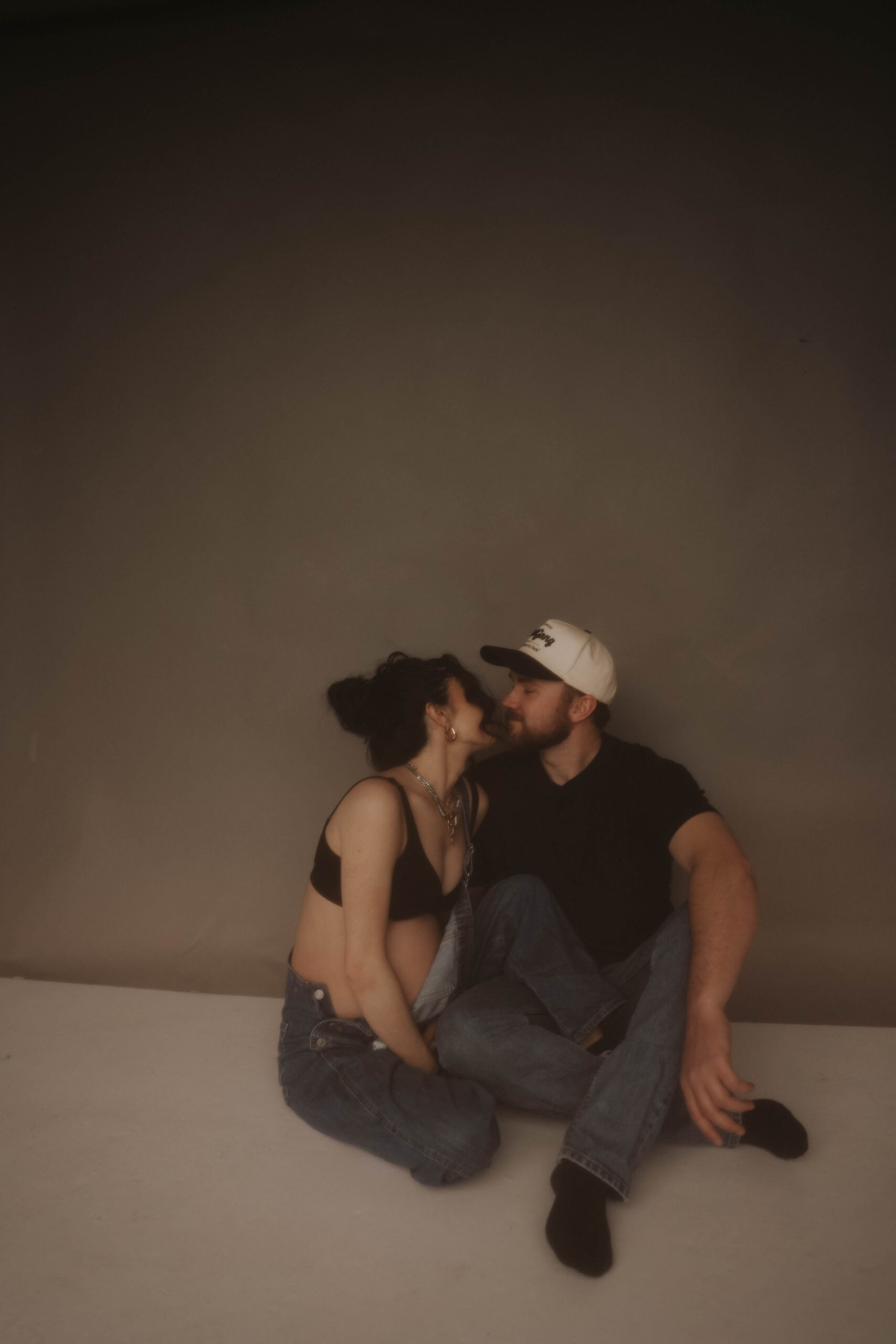 soon to be parents sitting on the floor smiling at each other during denver maternity photoshoot