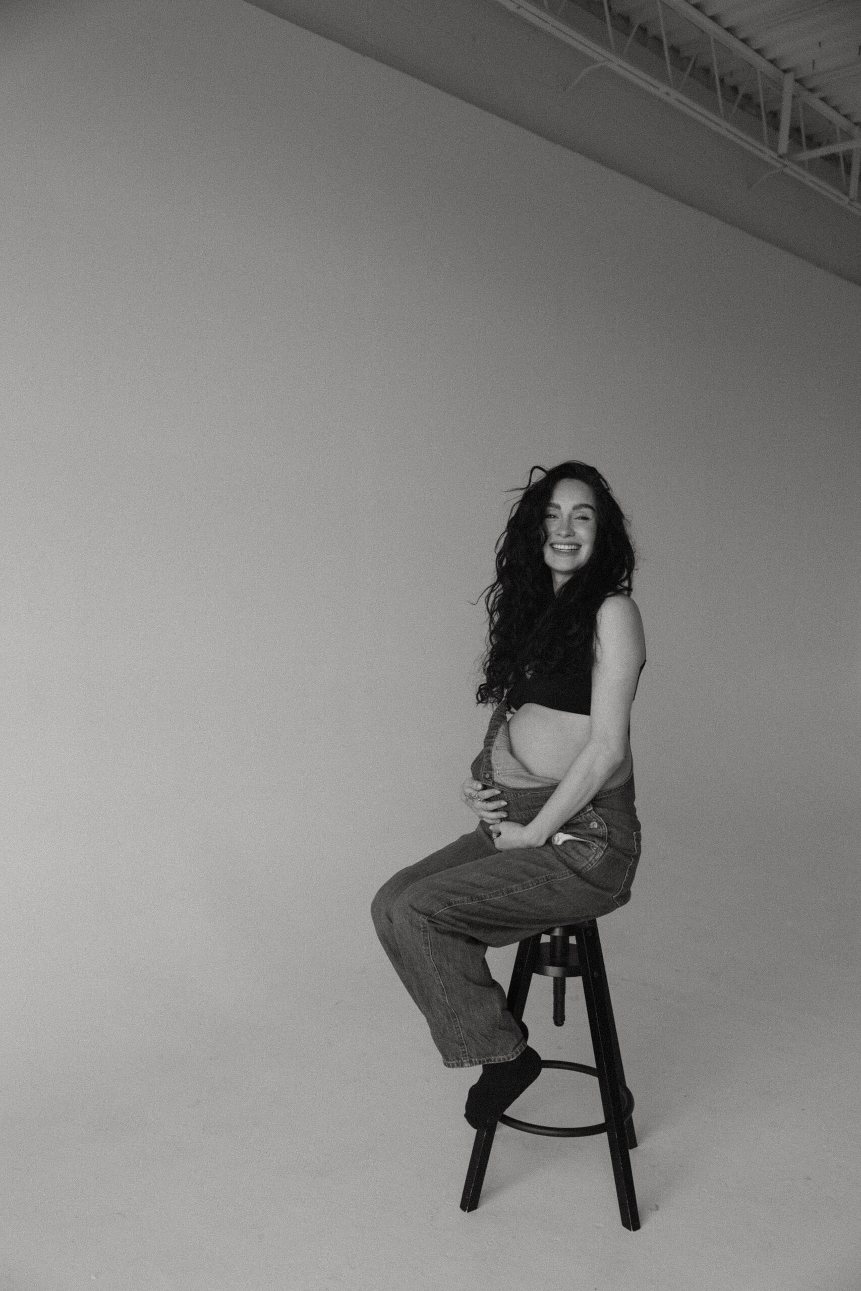 soon to be mama sitting on a stool holding her belly during a denver maternity photoshoot