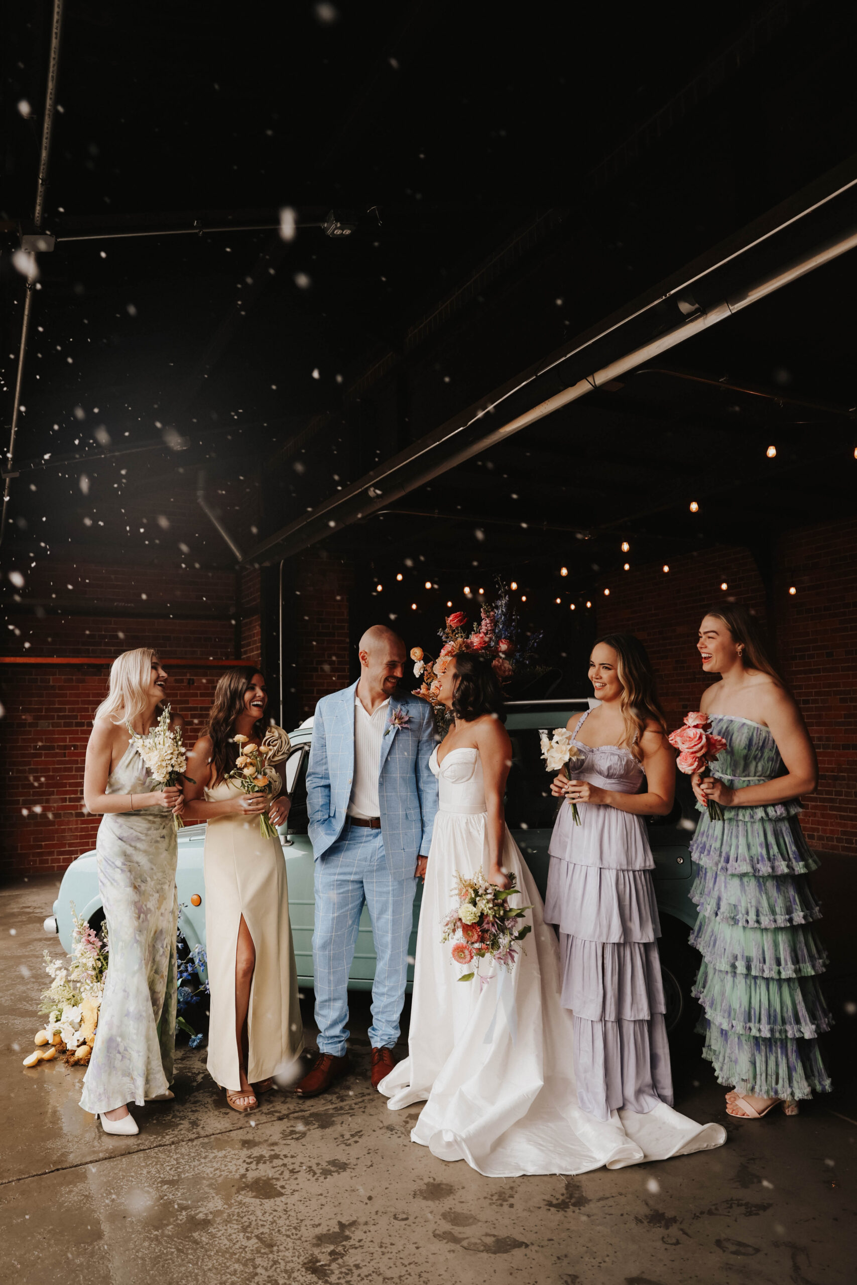 snow falling while the bride and groom pose with the bridesmaids during a colorful spring wedding 