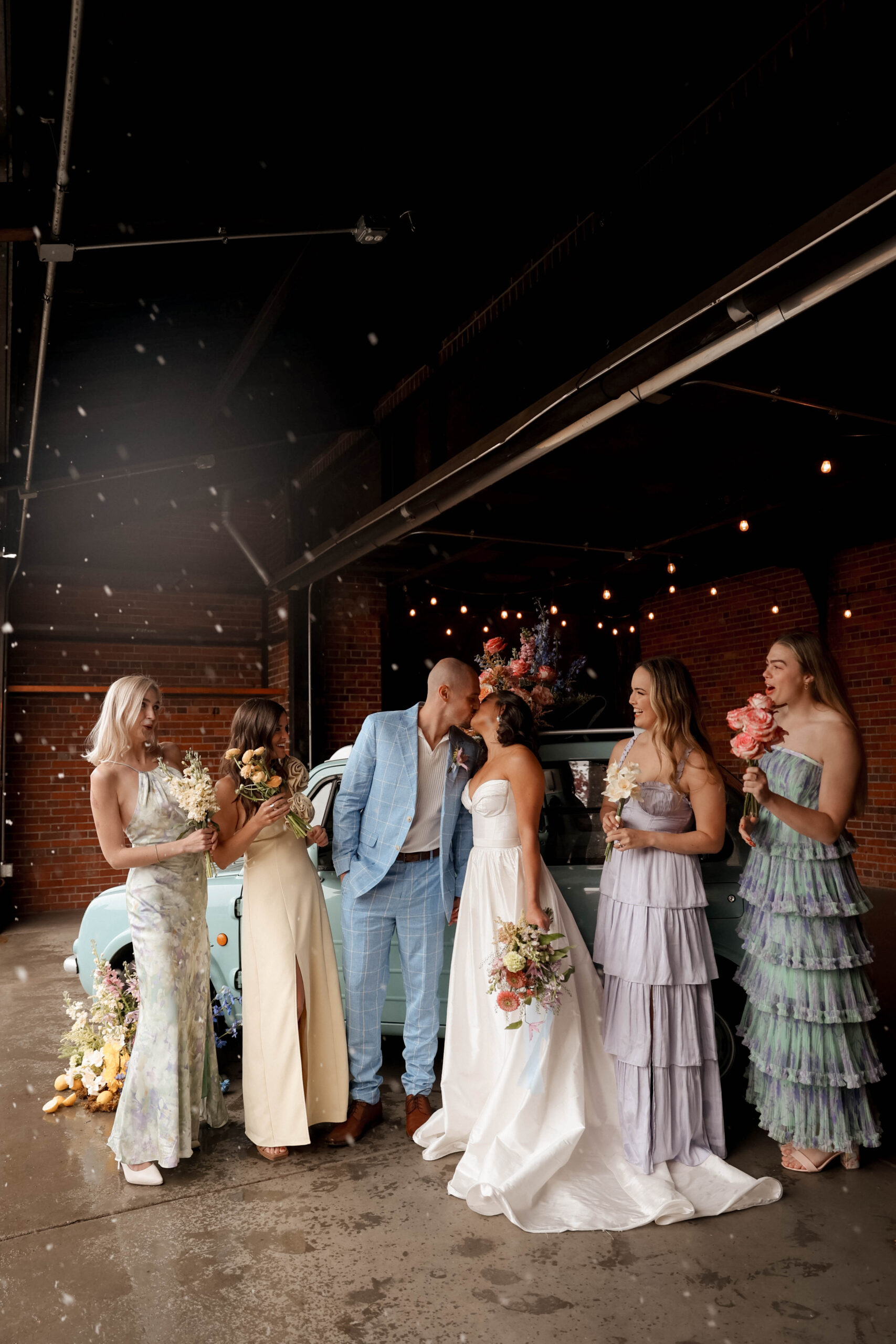 bride and groom kissing while mix matched bridesmaids stand around them 