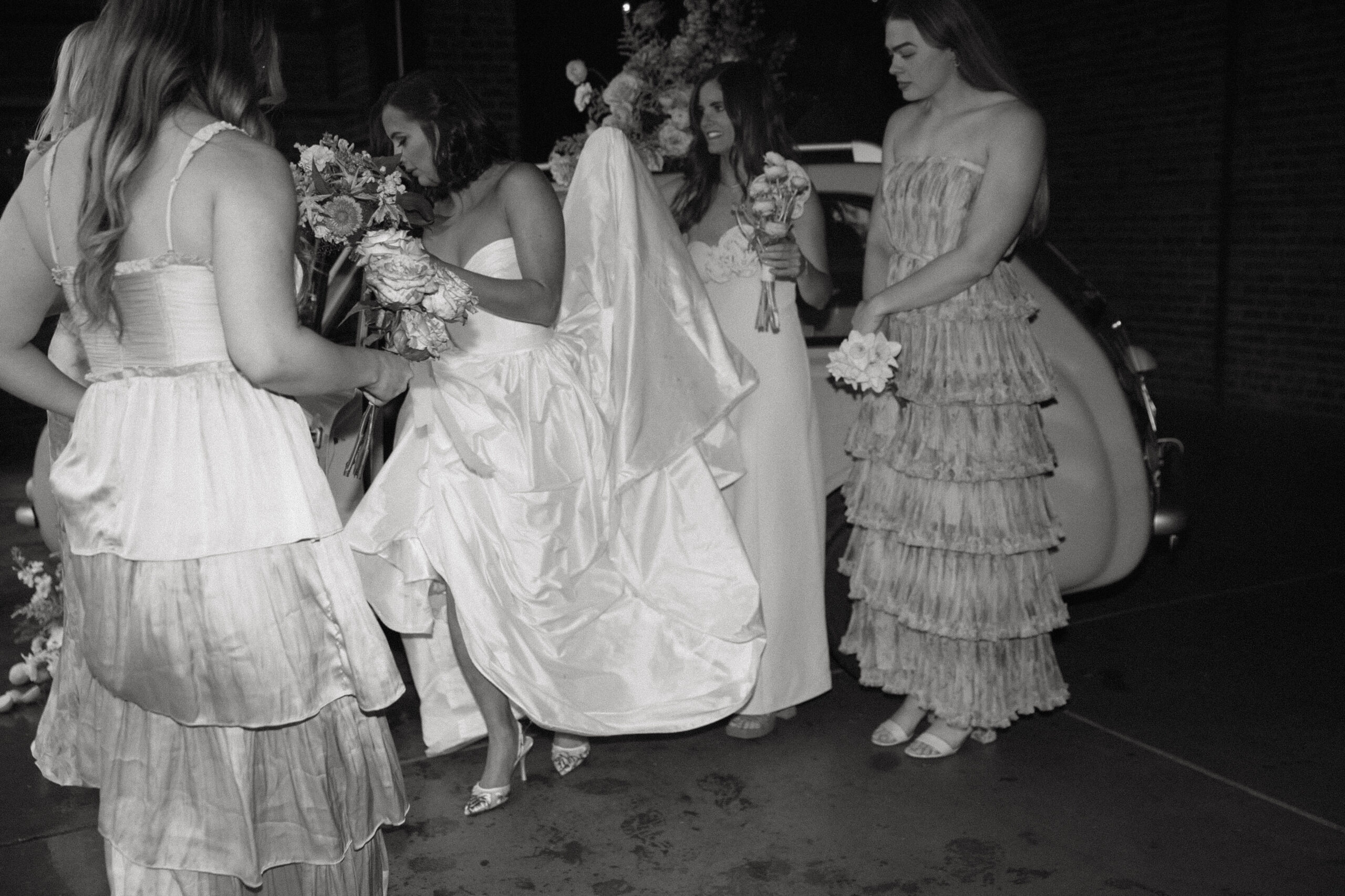 candid photo of bridesmaids helping bride with her dress