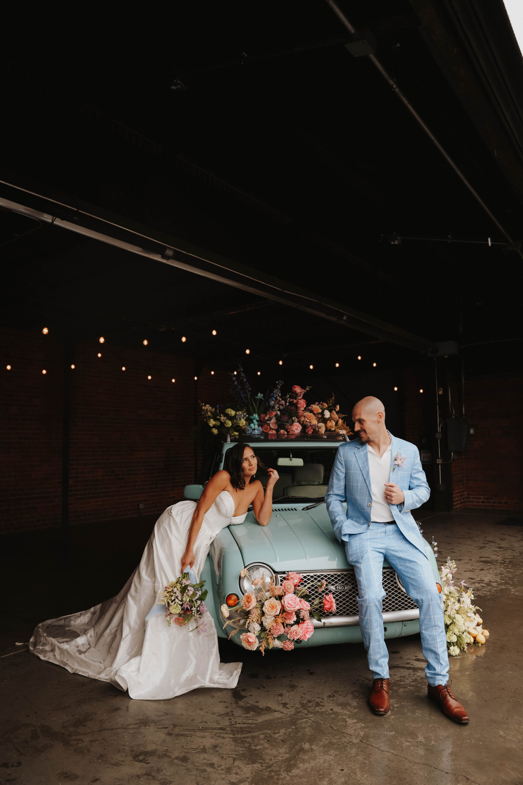 bride and groom posing on the blue floral styled car during a colorful spring wedding 