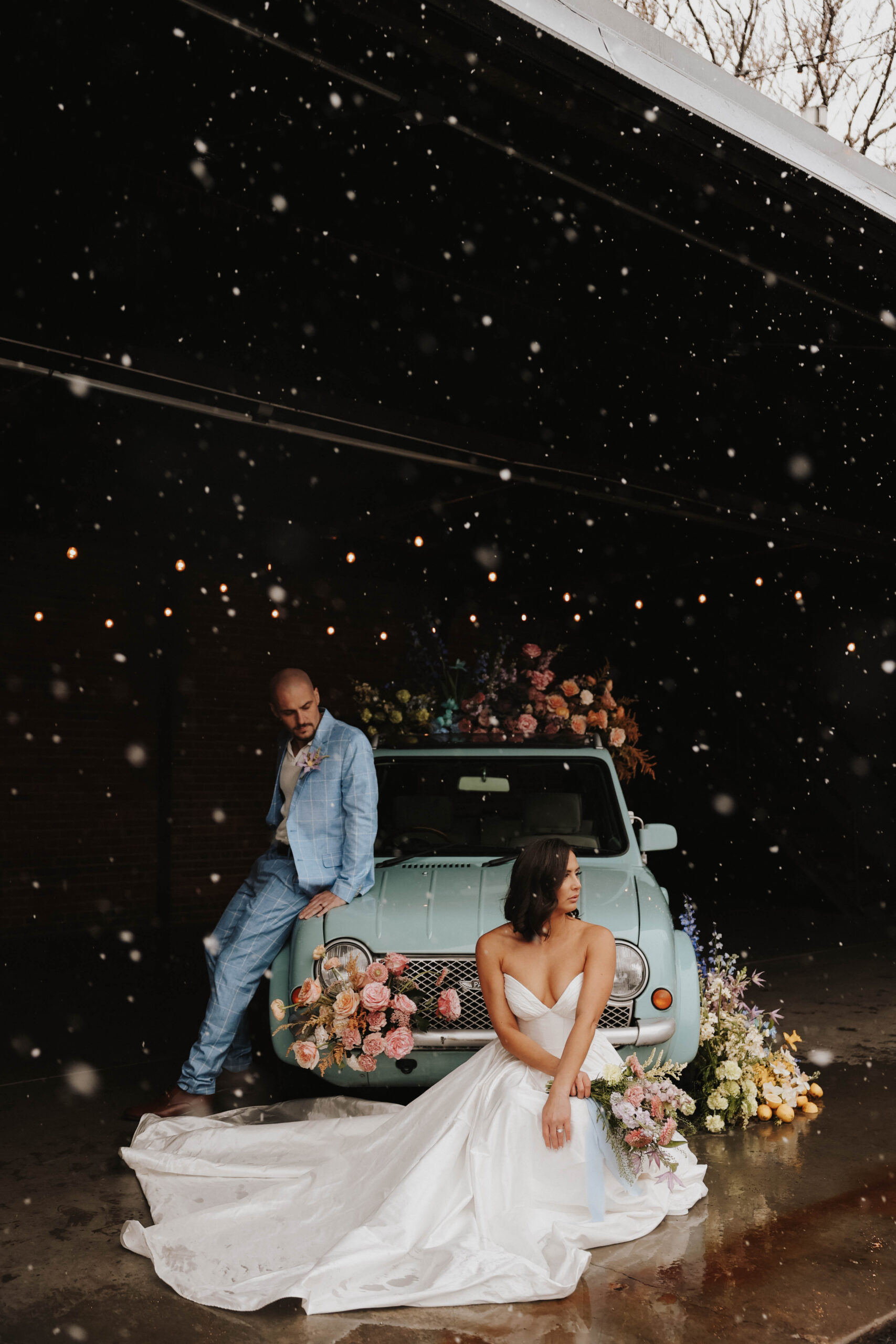 bride sitting in front of floral car and husband standing looking down at her during a colorful spring wedding 