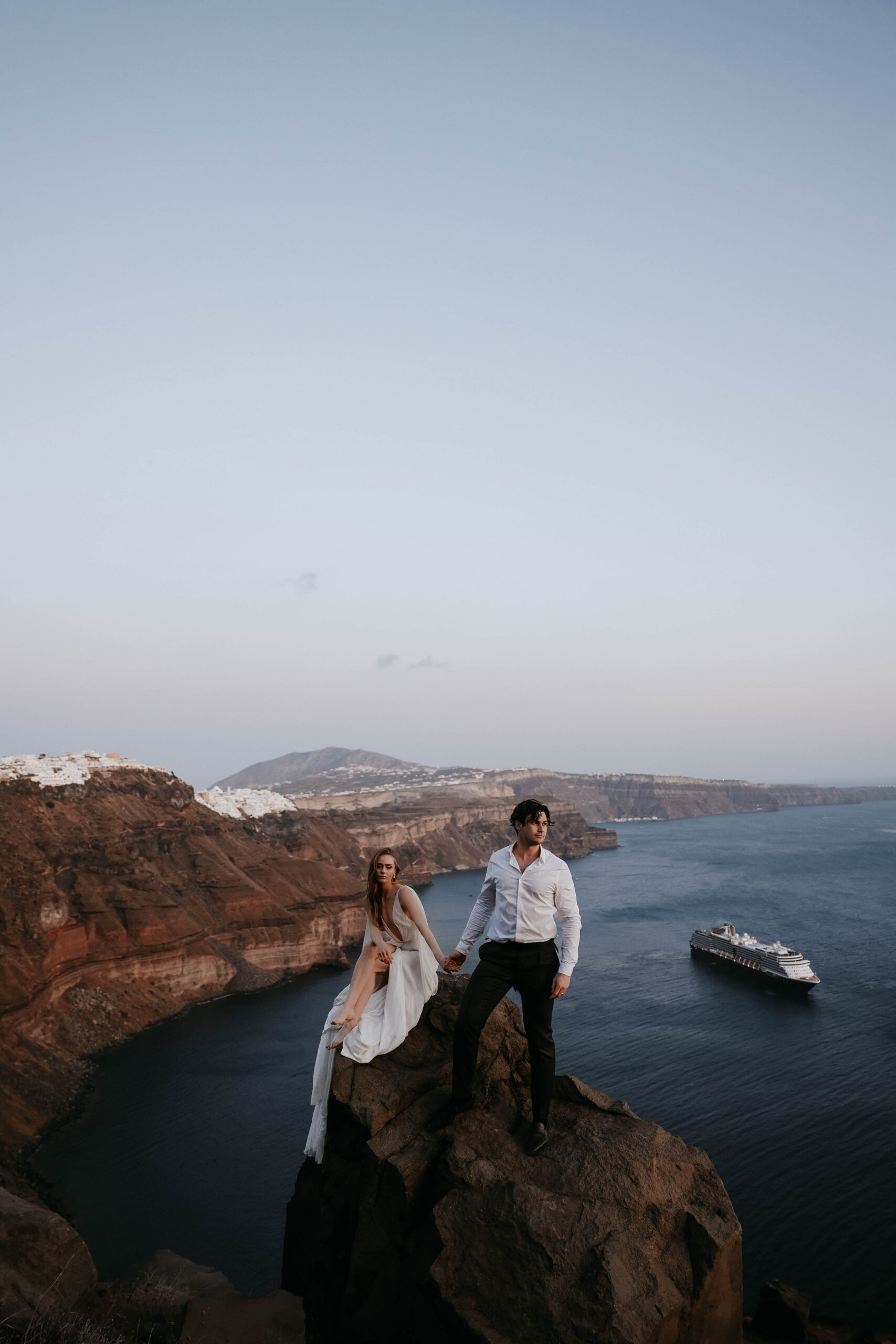 bride and groom holding hands with the sea and cliffs behind them during their Santorini Greece elopement