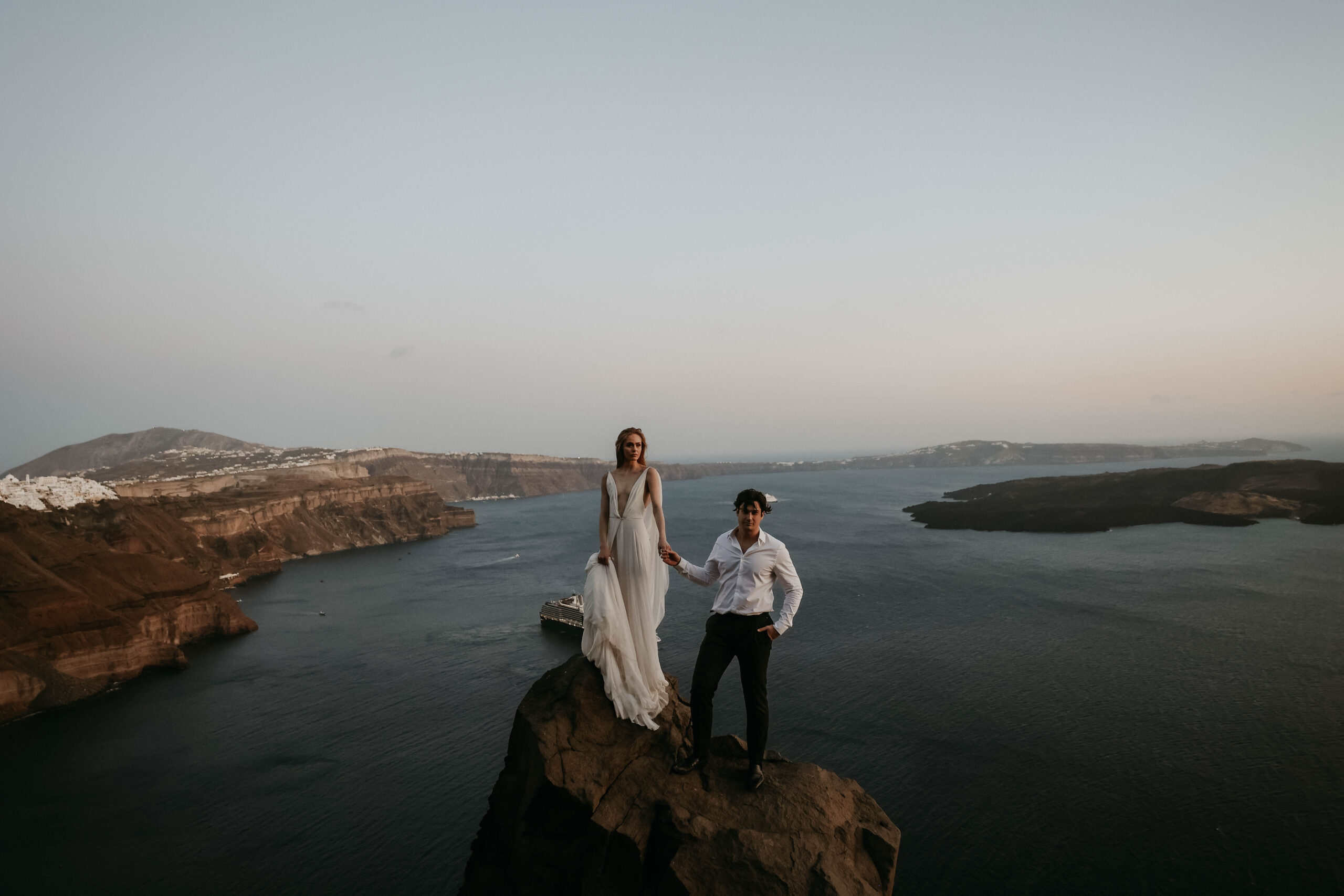 bride and groom standing on a cliff with an incredible ocean view behind them for Santorini Greece elopement