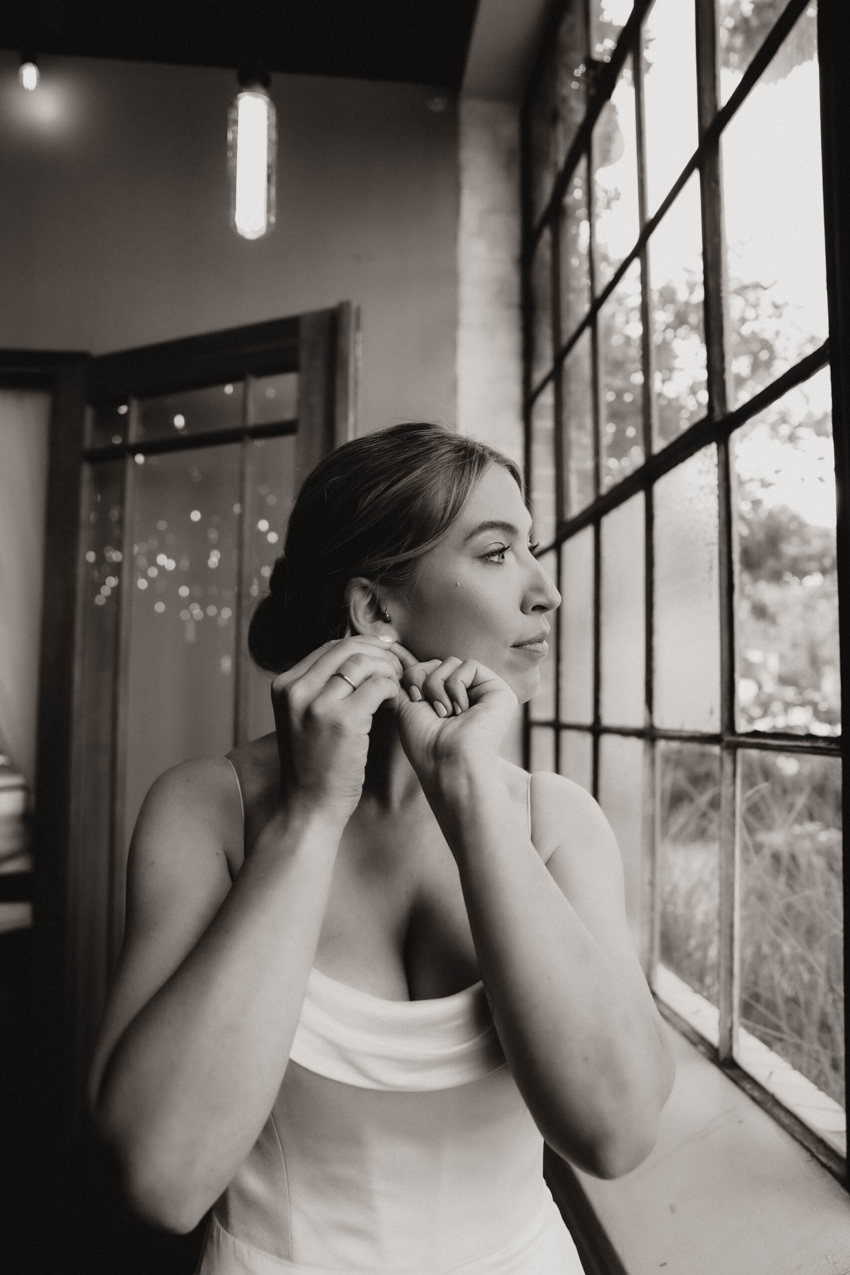 bride fixing her earrings by the window 