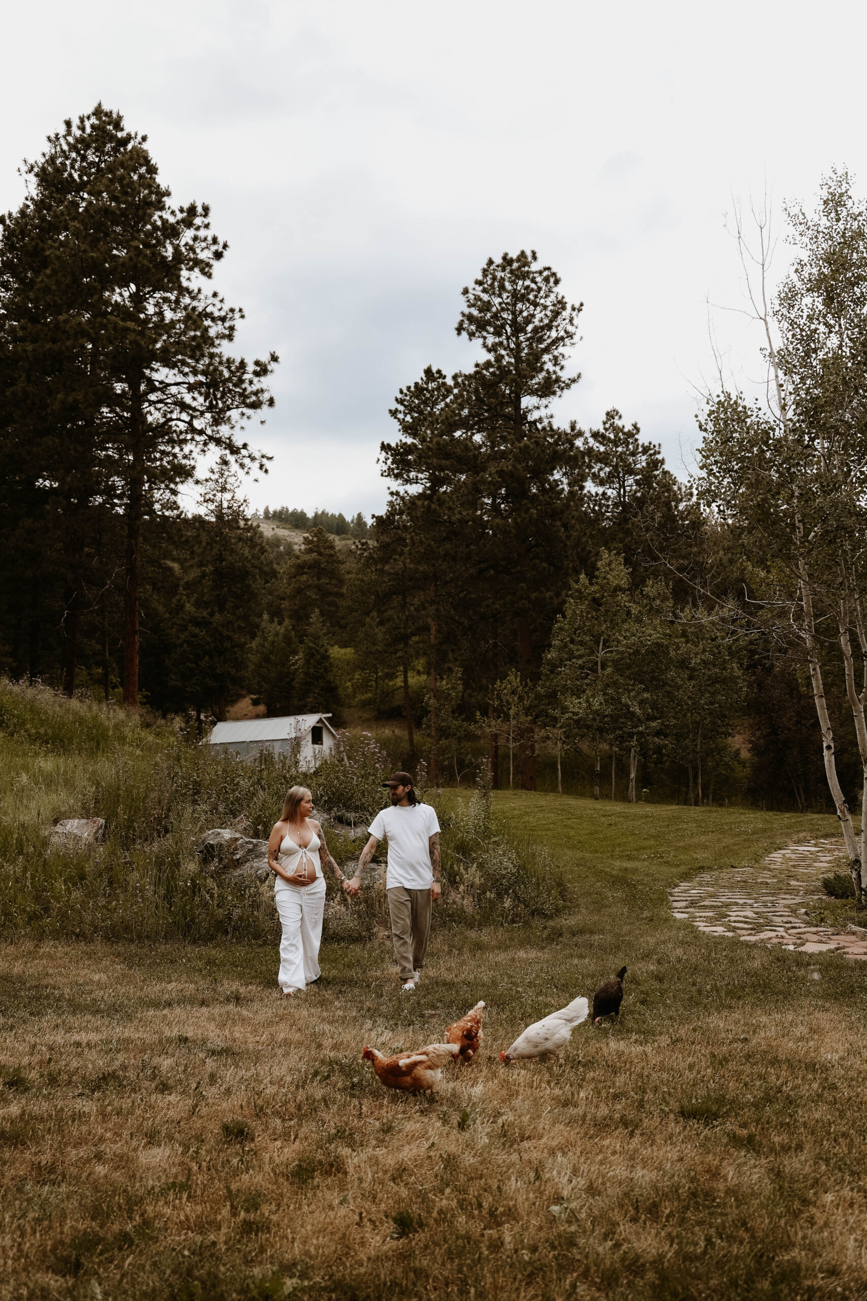 a couple holding hands in their backyard with their chickens during a Denver Maternity Photography session 