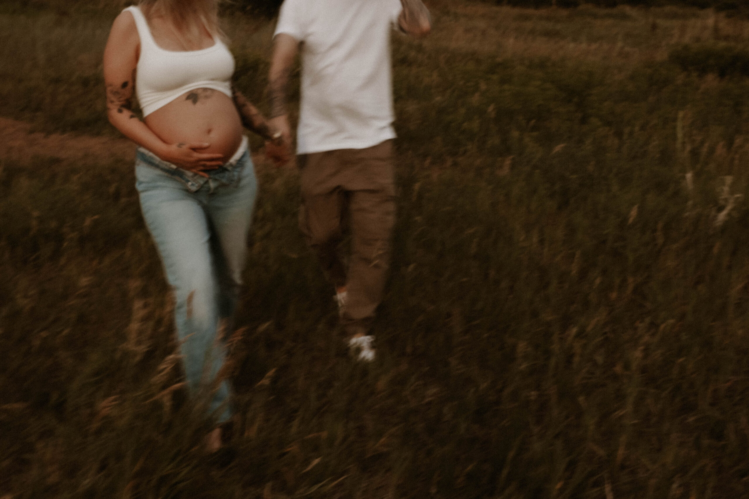 a couple holding hands, walking through the field during their Denver Maternity Photography session 