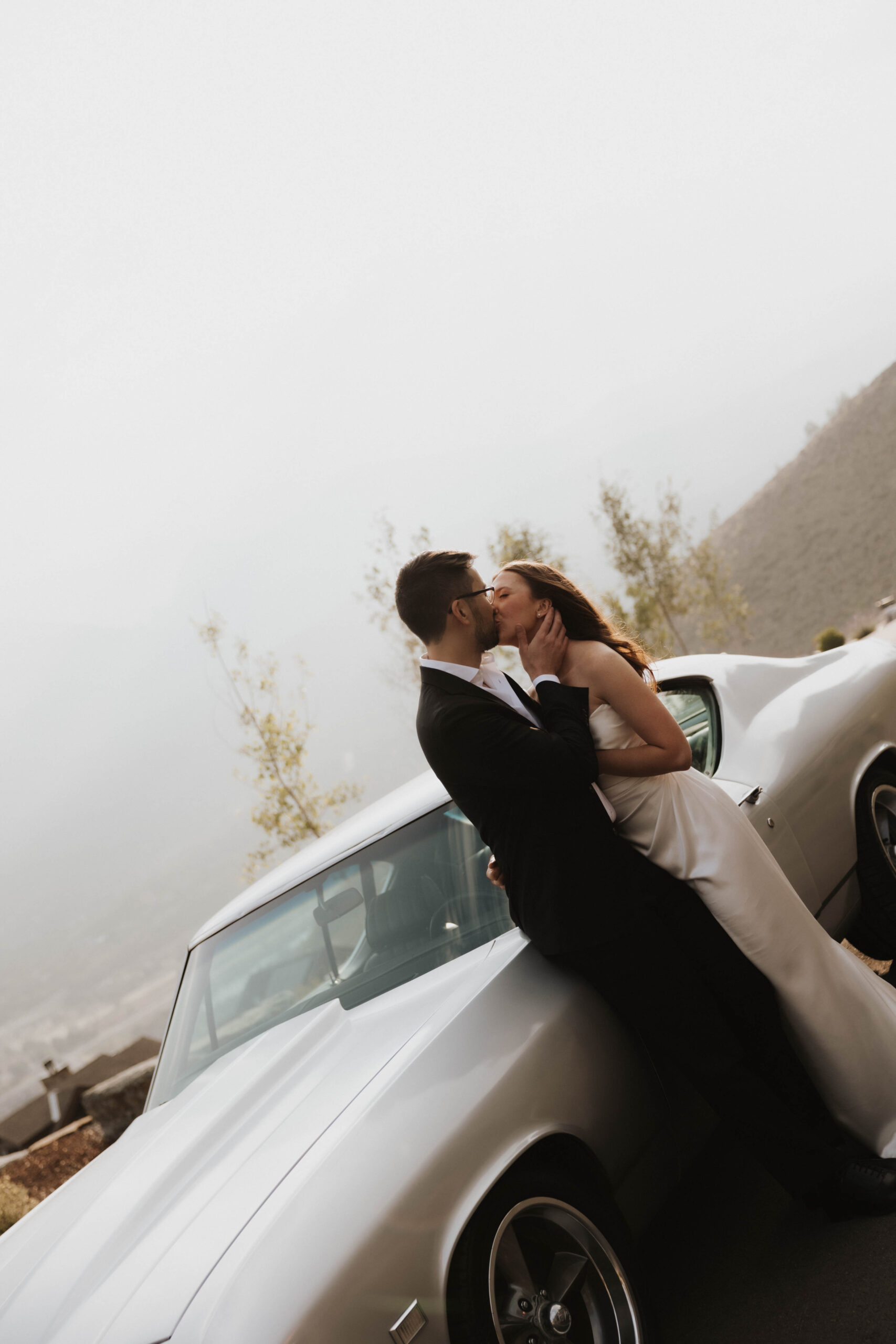 bride and groom kissing in front of a car 