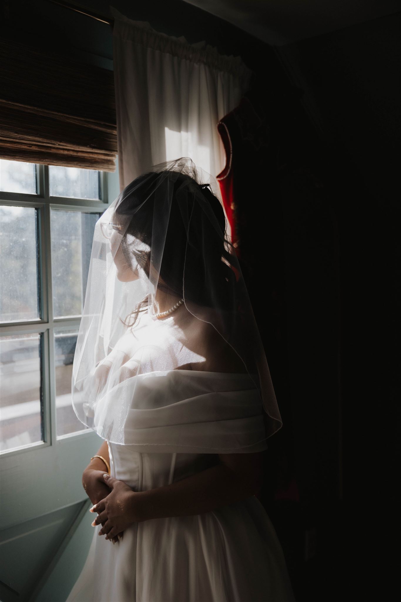 bride standing by the window with her veil over her head