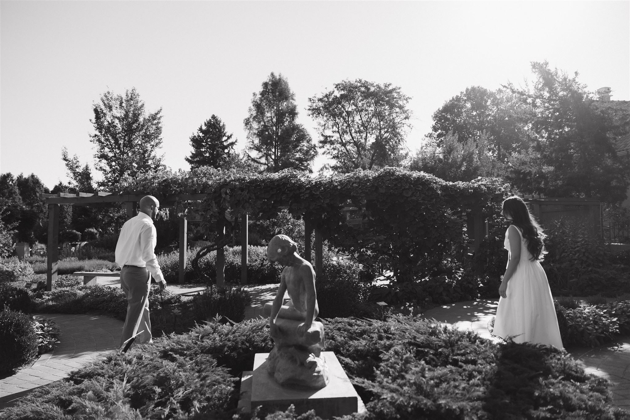 a couple walking towards each other by the statues in the garden 