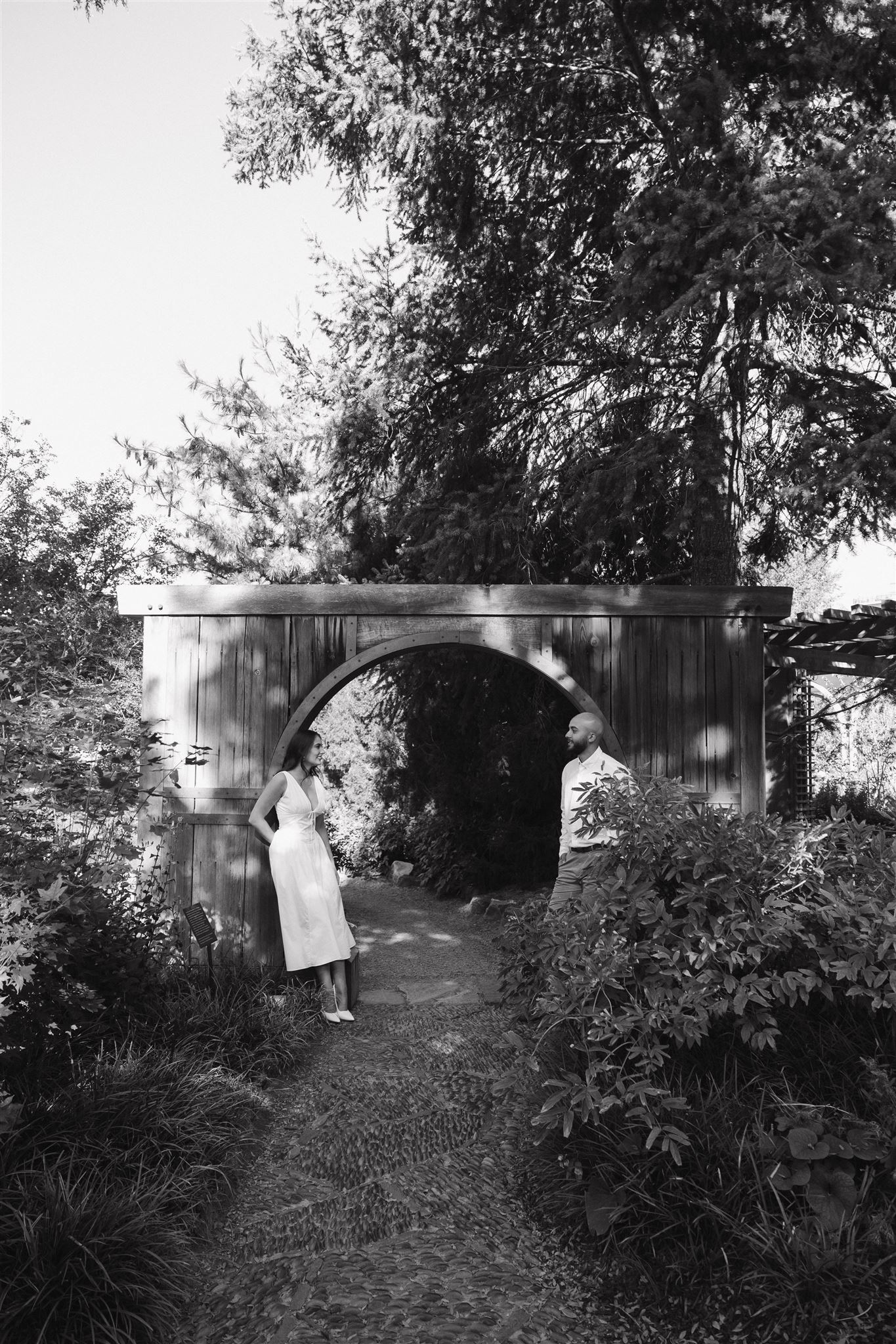 a couple standing on a pathway in a garden during their engagement session 