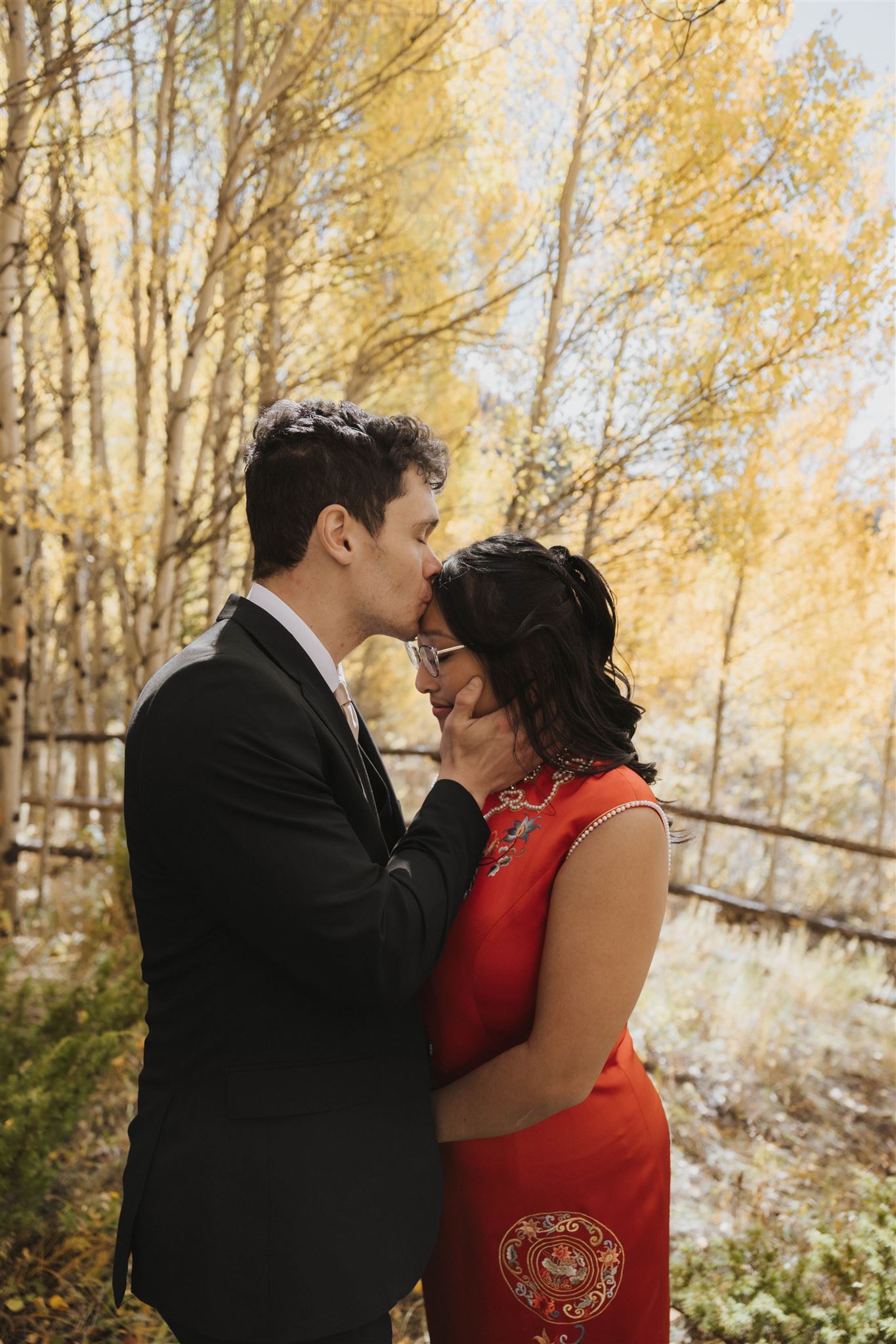 groom kissing bride on the forehead in the woods 