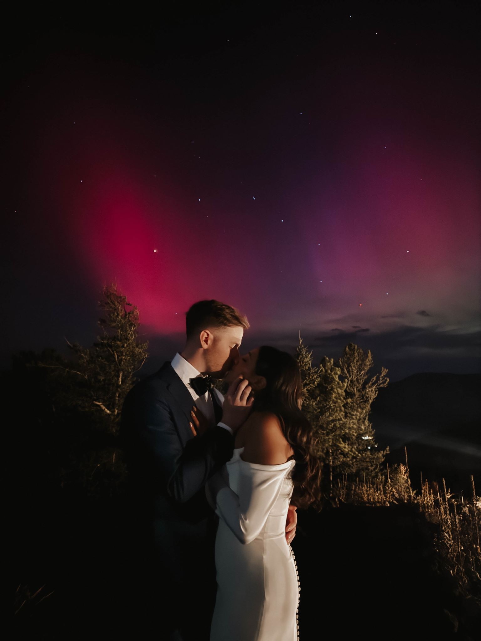 bridal couple kissing with the northern lights above them 