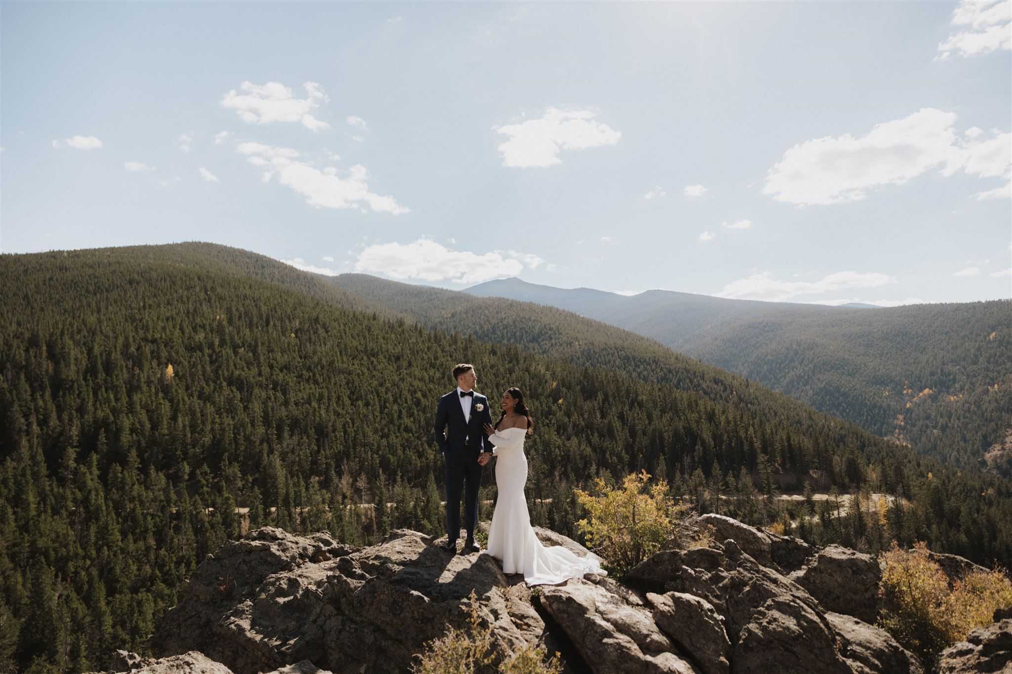 bride and groom standing on a rock with the mountains behind them 