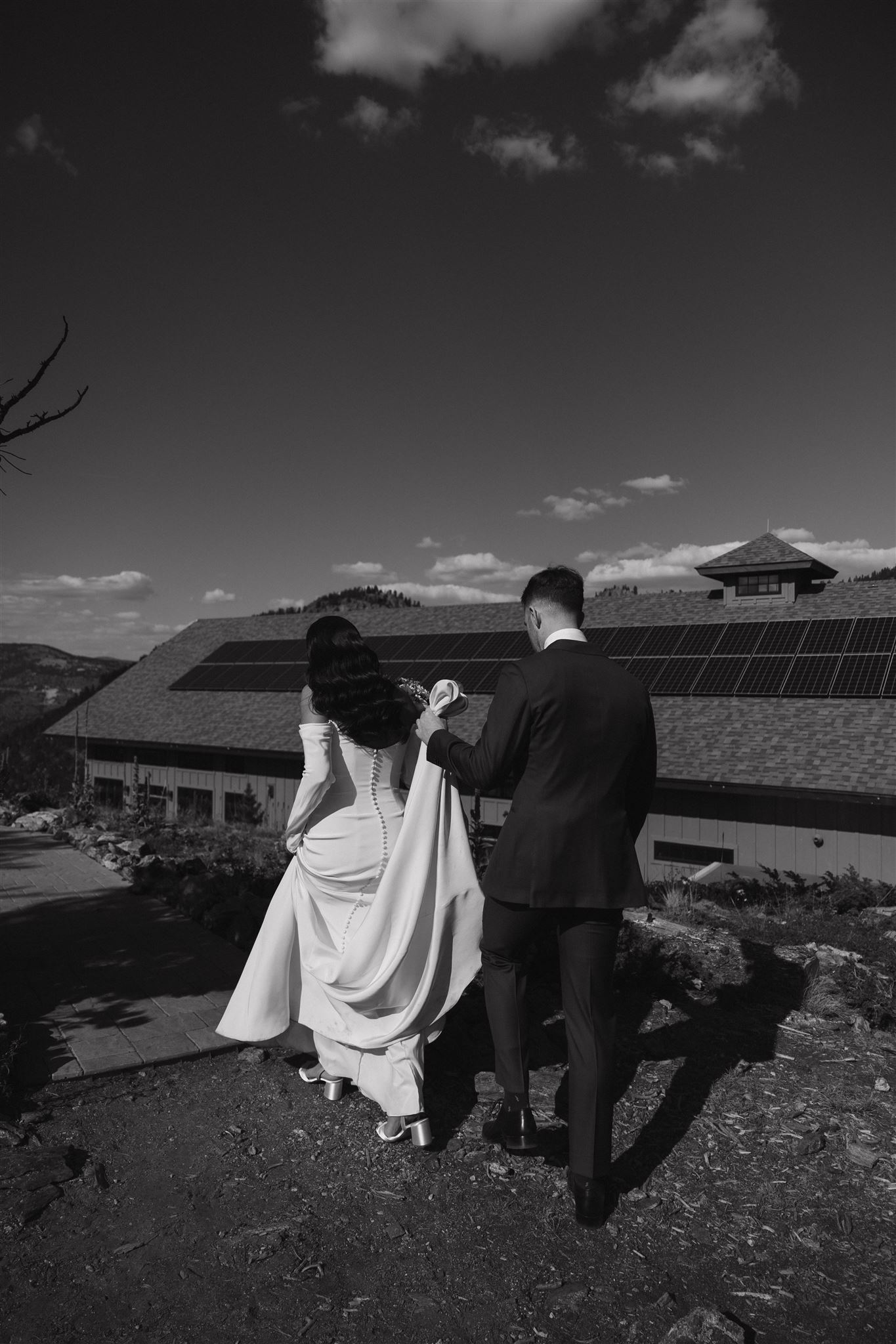 groom holding the bride's dress as she walks 