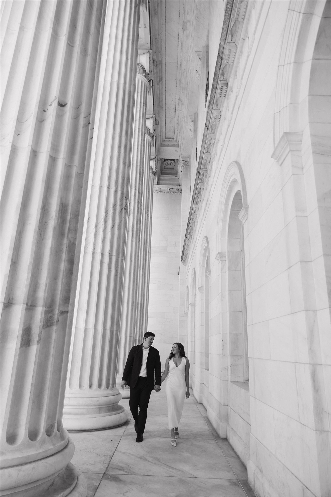 a black and white photo of a couple holding hands and walking outside the courthouse 