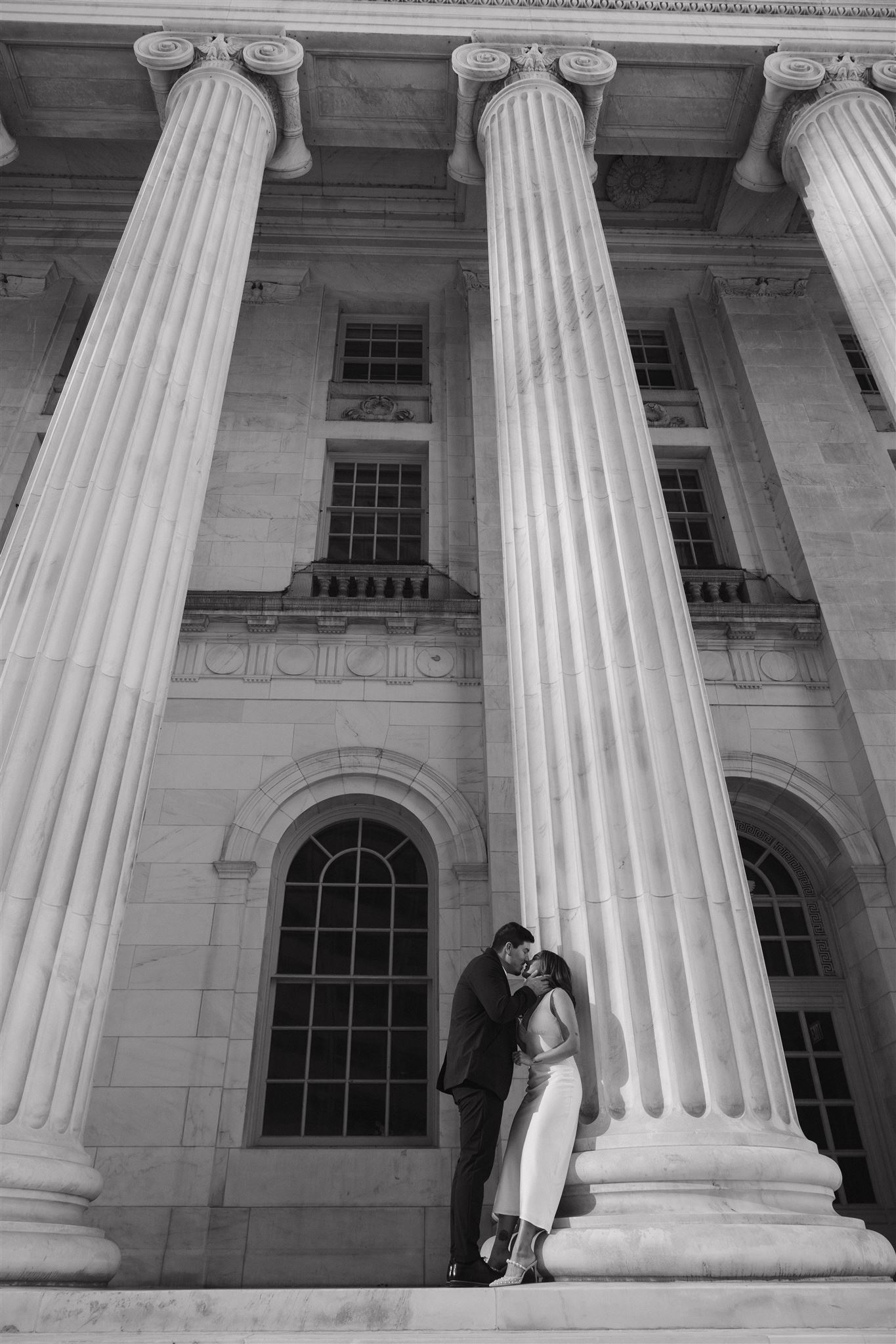 a man and woman kissing against a grand white pillar for their Elegant Engagement Photos