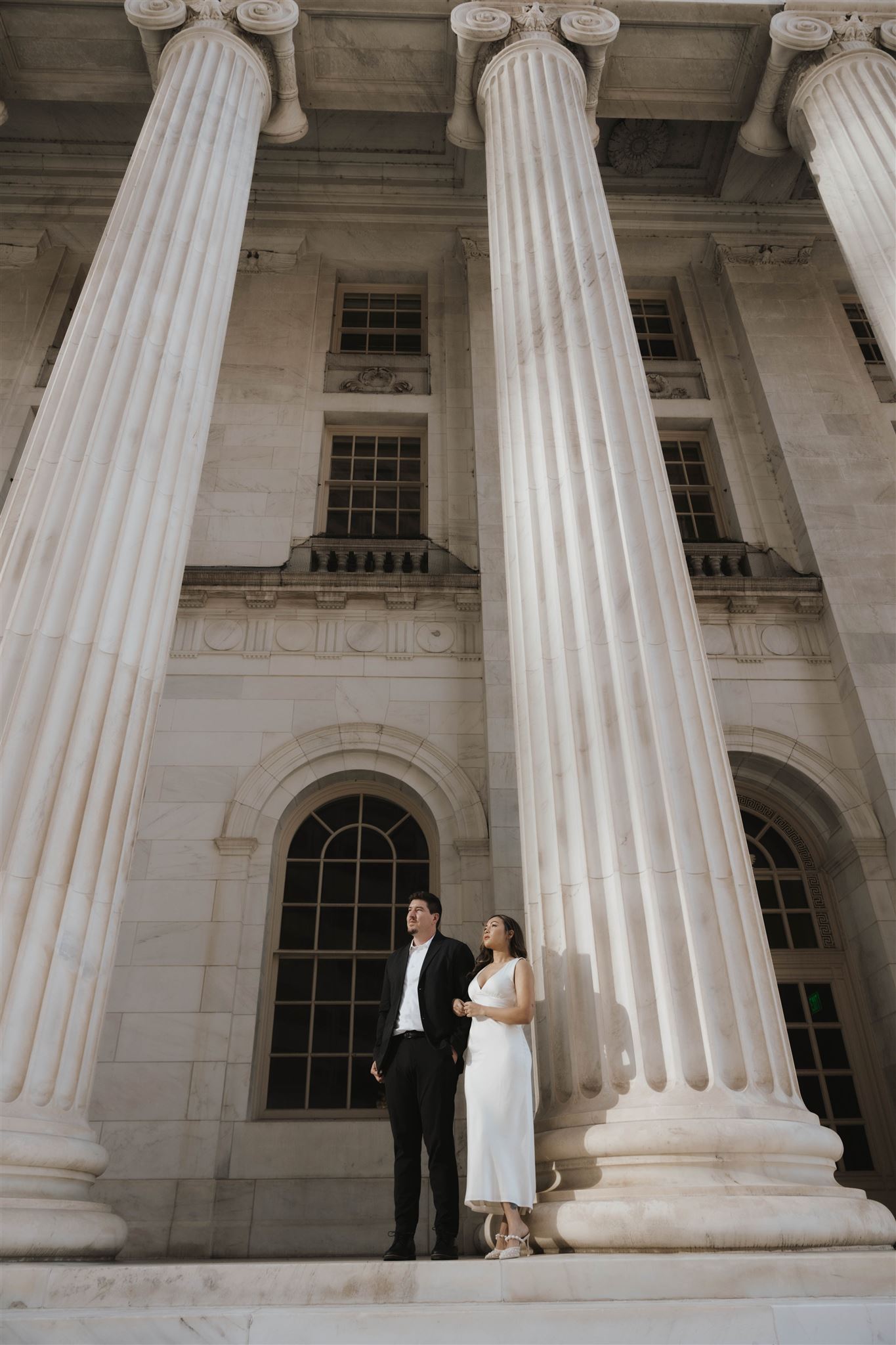 a man and woman standing by the courthouse pillars looking into the distance 