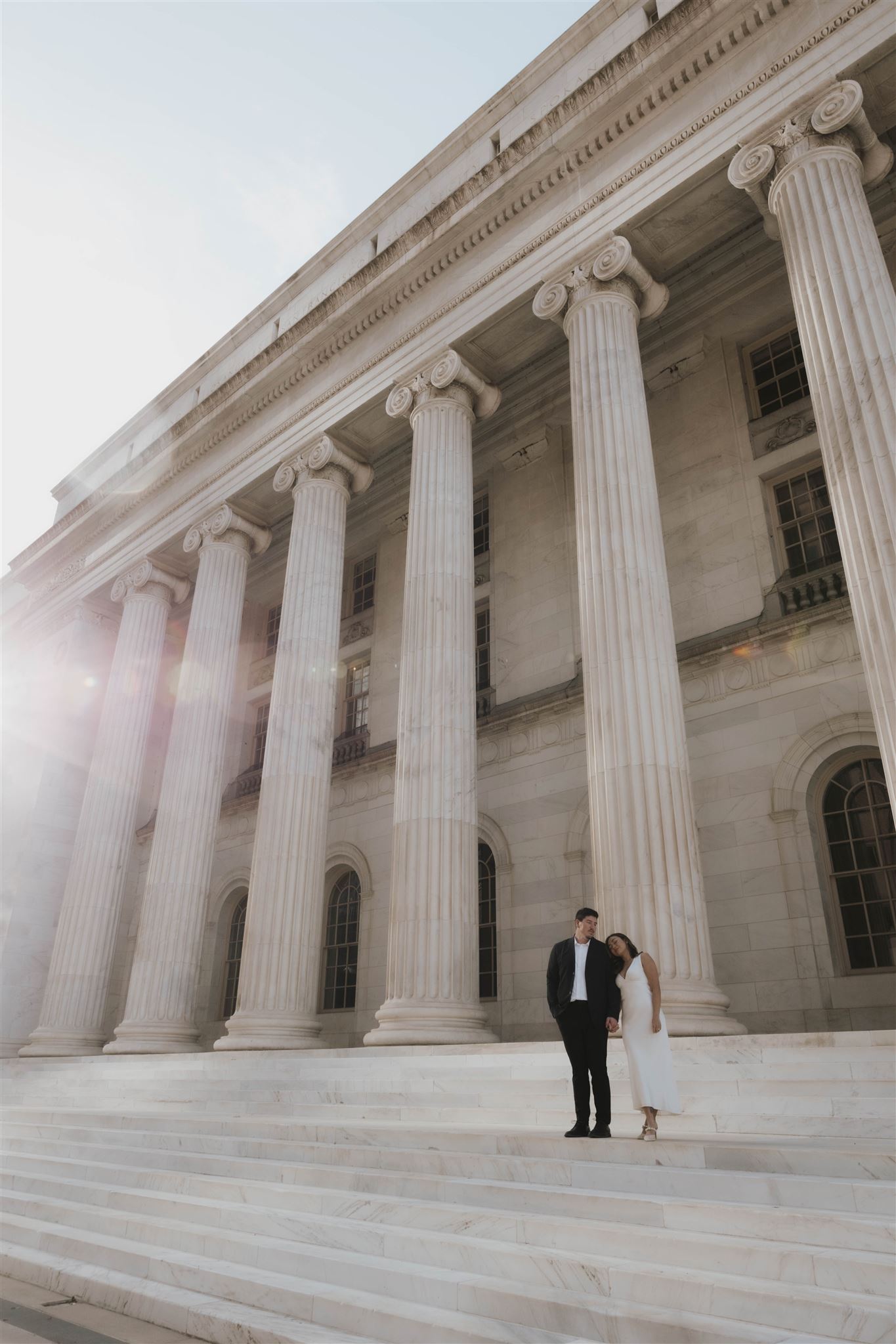 newly engaged couple standing on the courthouse steps as the sun shines on them 