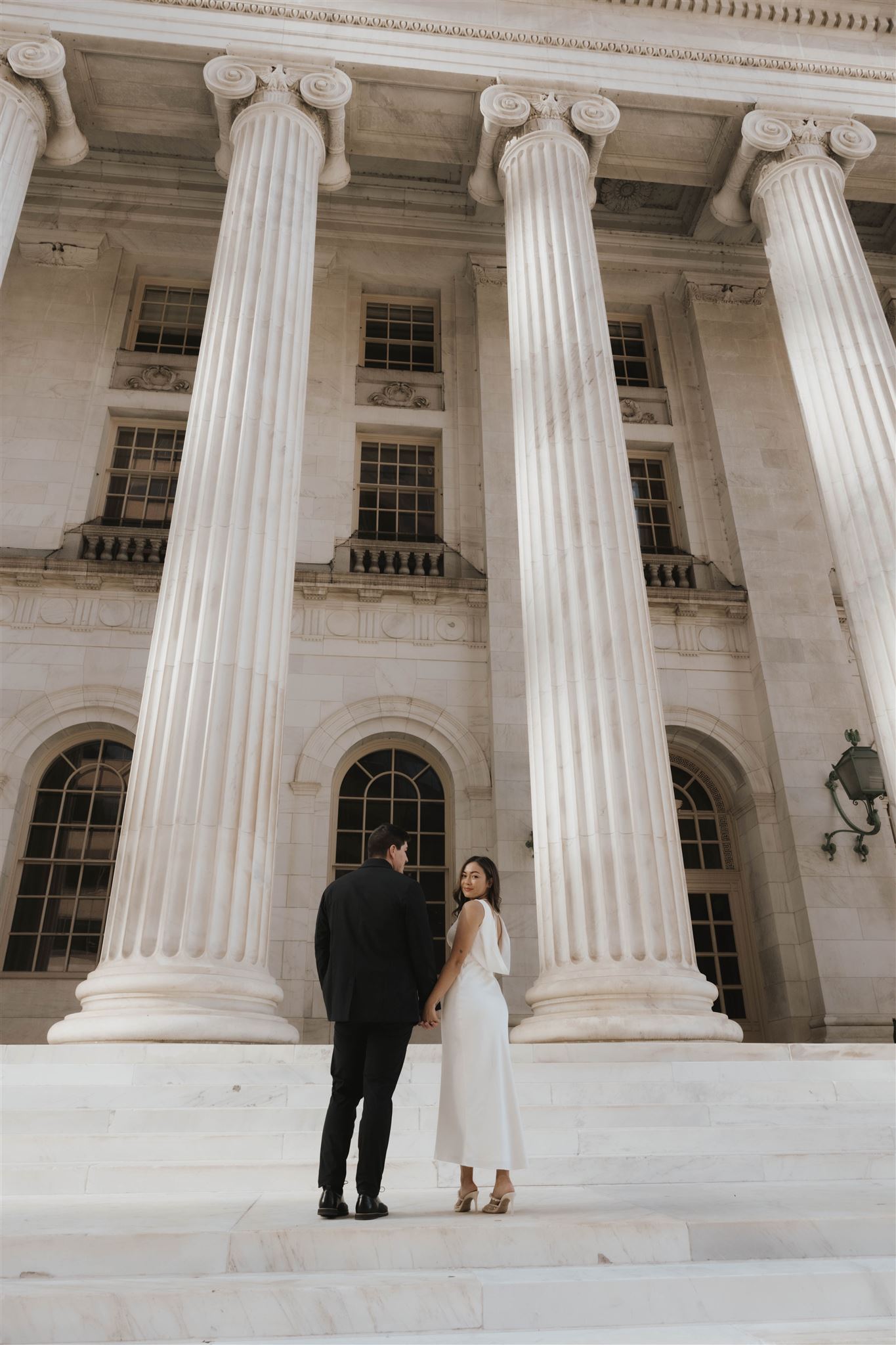 a couple holding hands with their back towards the camera on the courthouse steps for their Elegant Engagement Photos